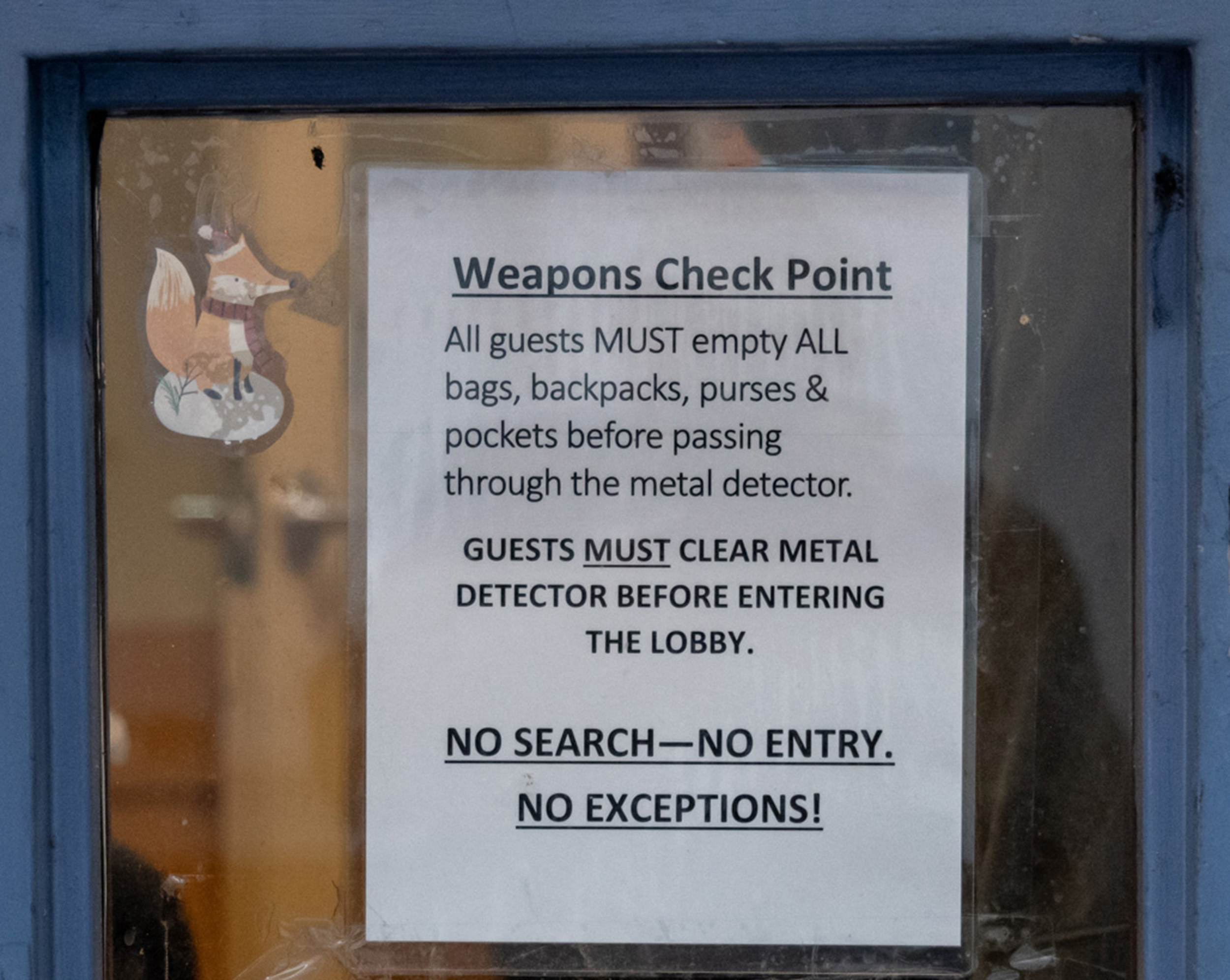 A sign on a window instructs guests to empty bags and clear a metal detector before entering. It states, &quot;No search—No entry. No exceptions!&quot; Decor features a small fox.