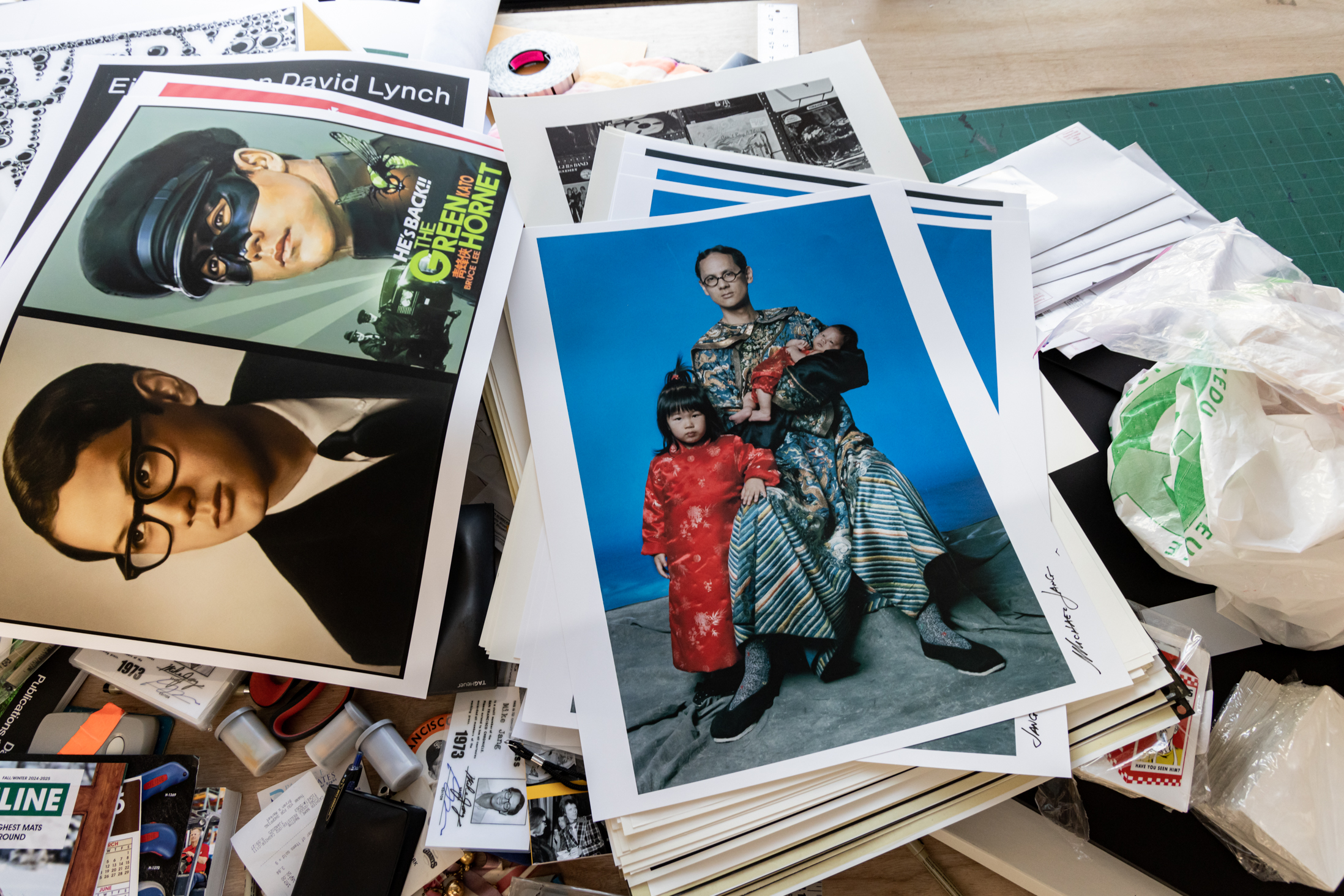 The image shows a cluttered desk with photographs, including a portrait of three people in colorful attire, along with various papers and office supplies.