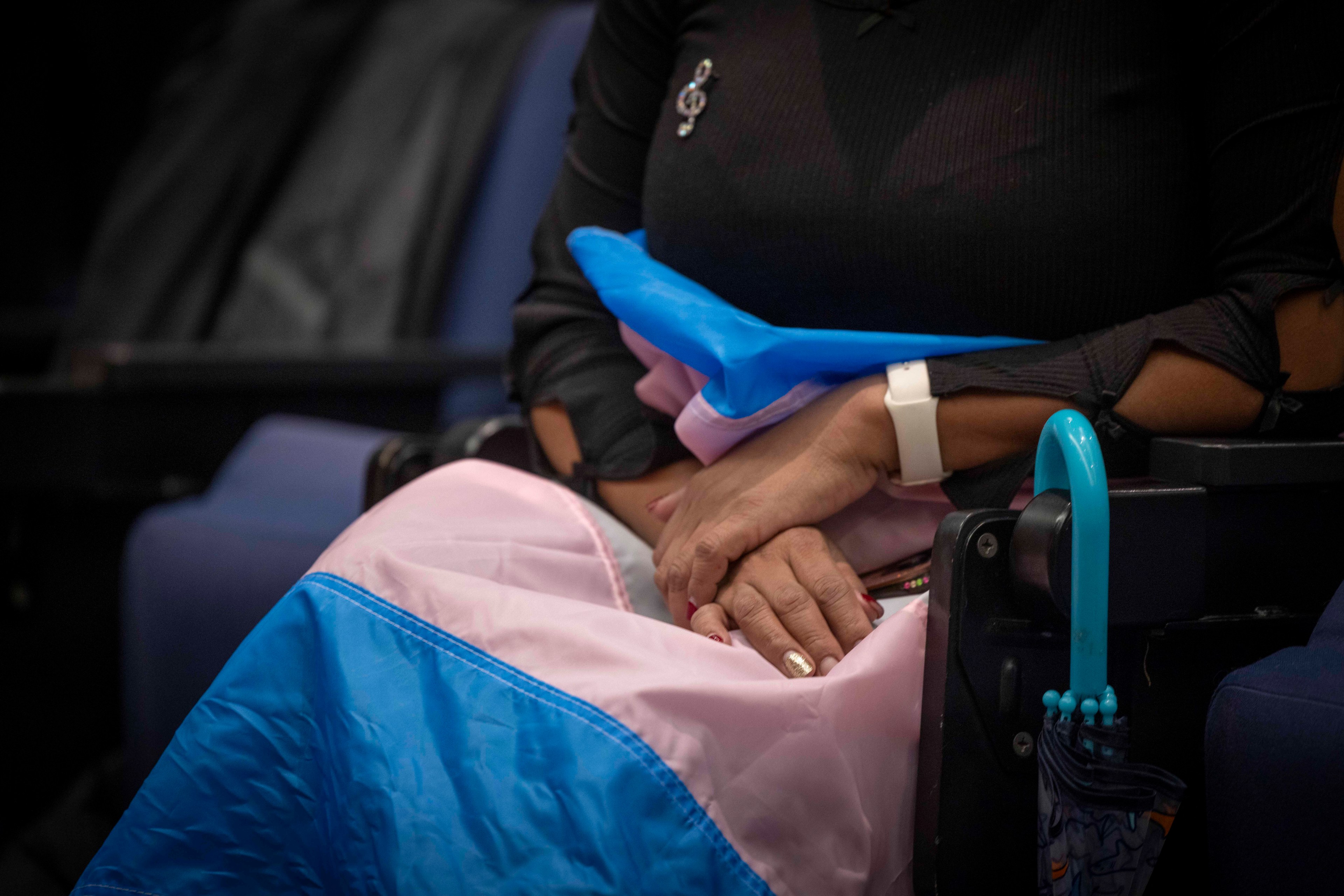 A closeup of hands draped over a transgender community flag on someone's lap.