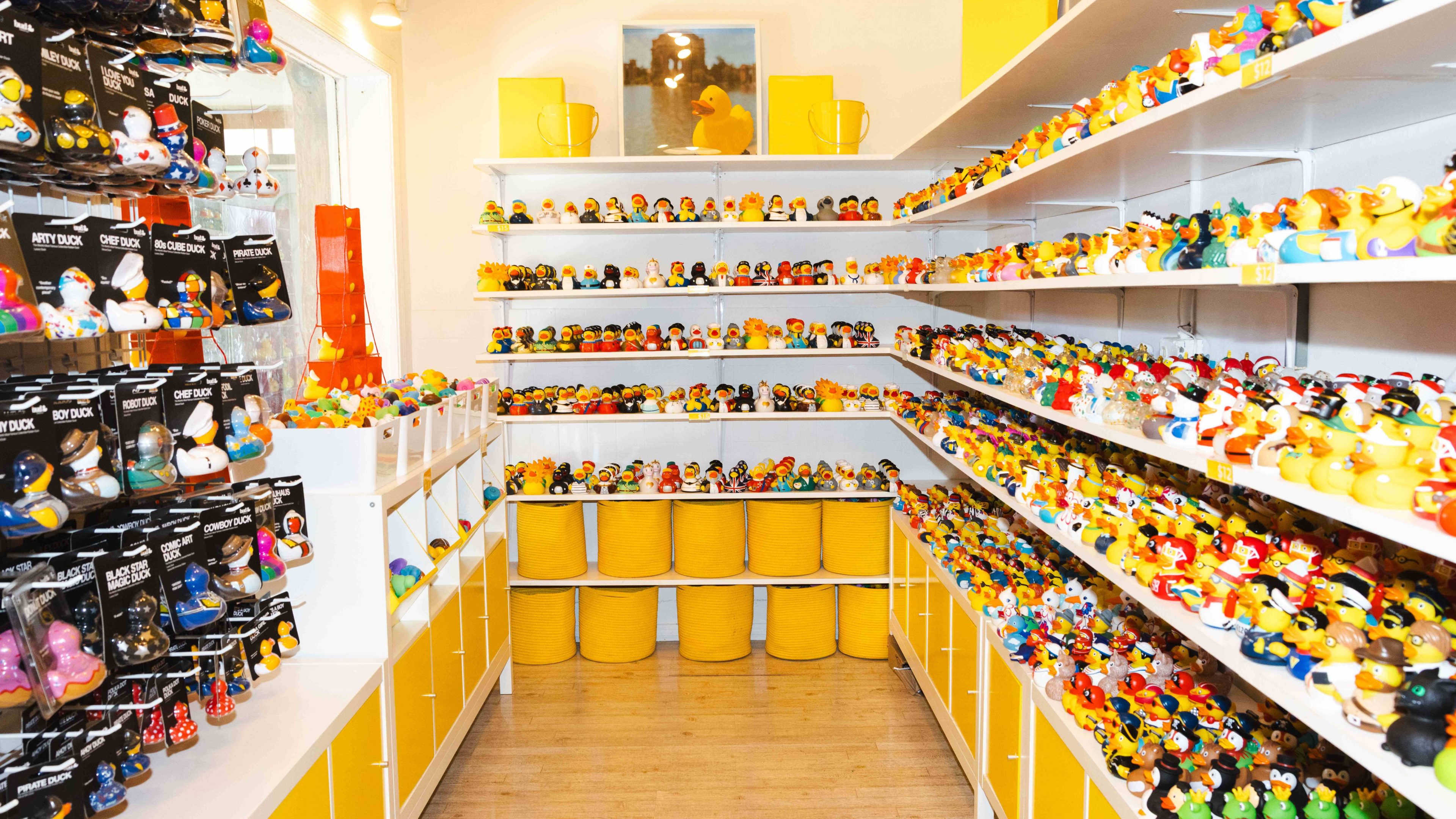 The image shows a store filled with shelves of colorful rubber ducks in various designs. The cubbies beneath and baskets on the floor are bright yellow.