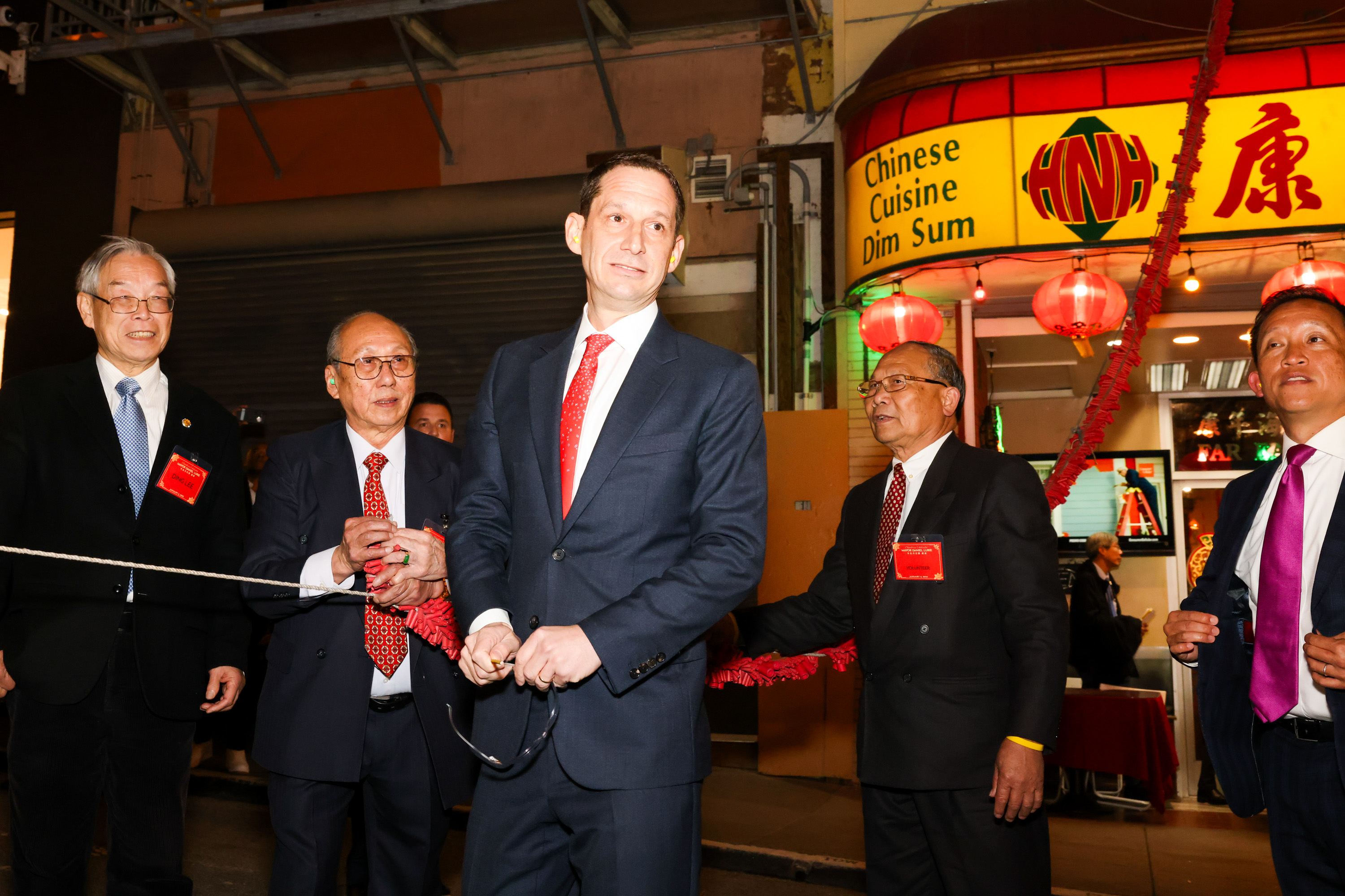 A group of men in suits stand in front of a Chinese restaurant, under a lit sign reading &quot;Chinese Cuisine Dim Sum.&quot; They appear to be at an event.