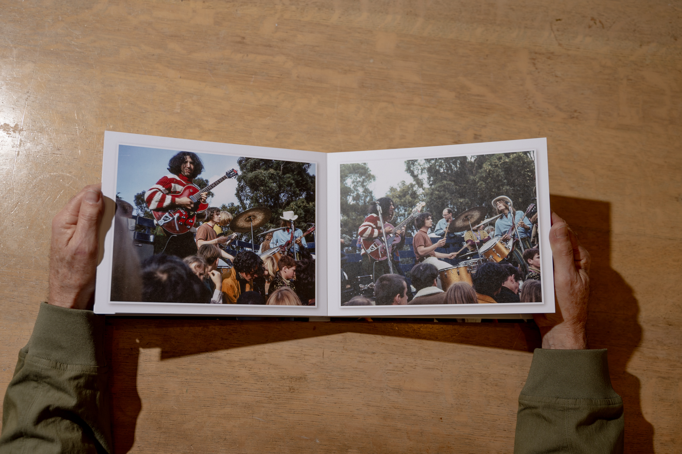 The image shows an open book with photos of a rock band performing outdoors. Musicians play guitars and drums, surrounded by an audience. Hands hold the book.