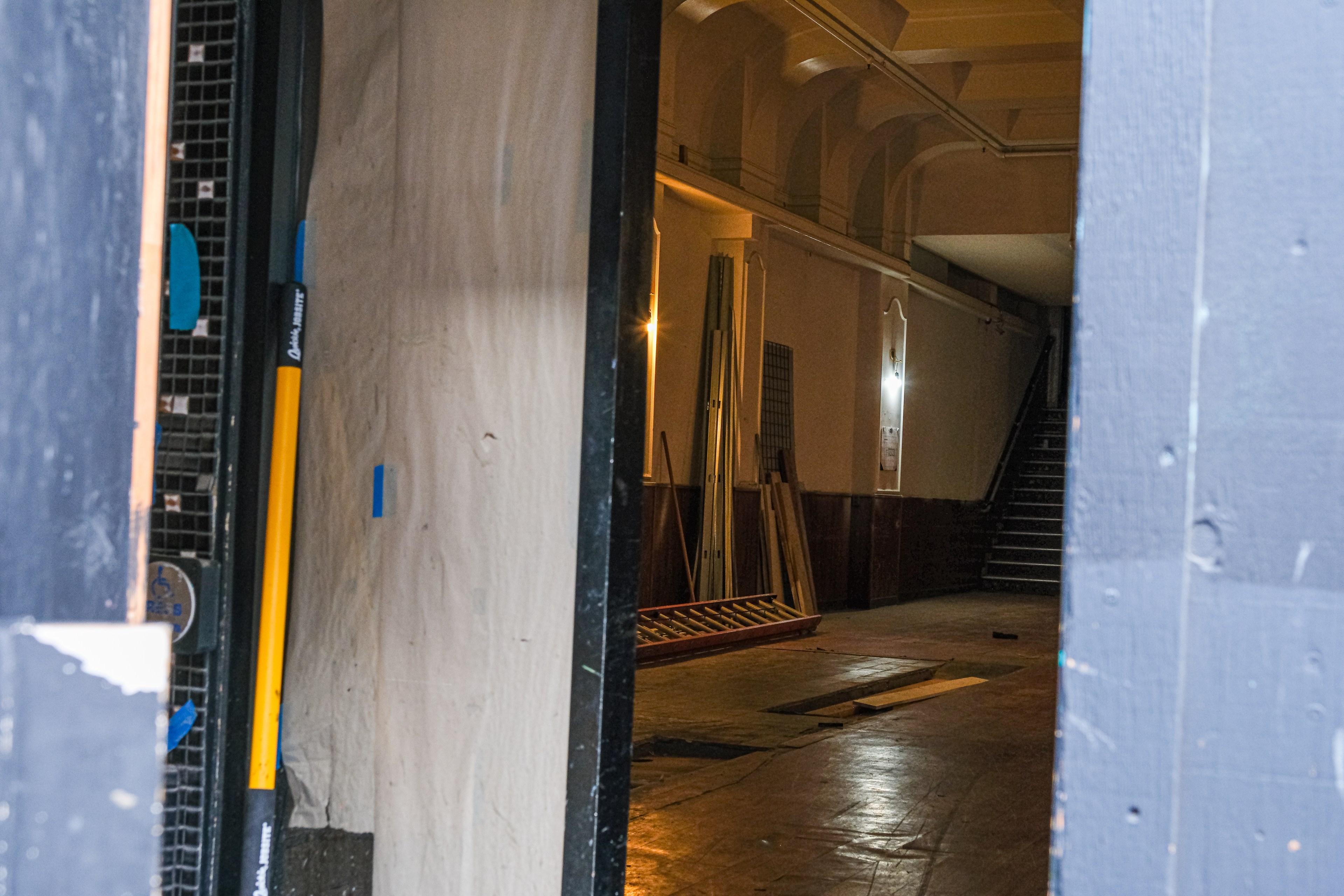 The image shows a partially open door leading to a dimly lit hallway under construction, with stacked materials and tools visible inside.