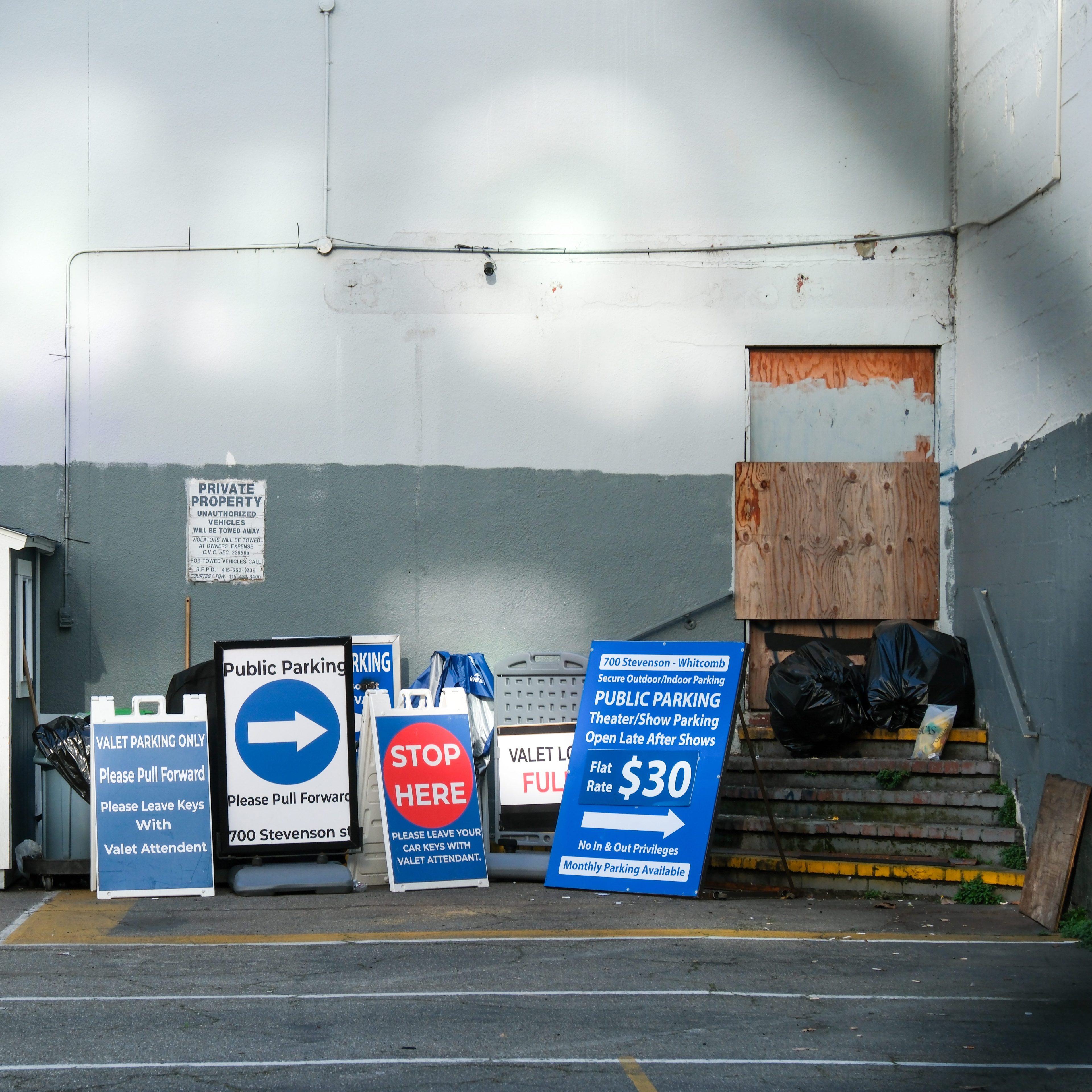 A parking lot entrance has various signs, including a blue one for public parking at a flat rate of $30, and another indicating valet parking only.