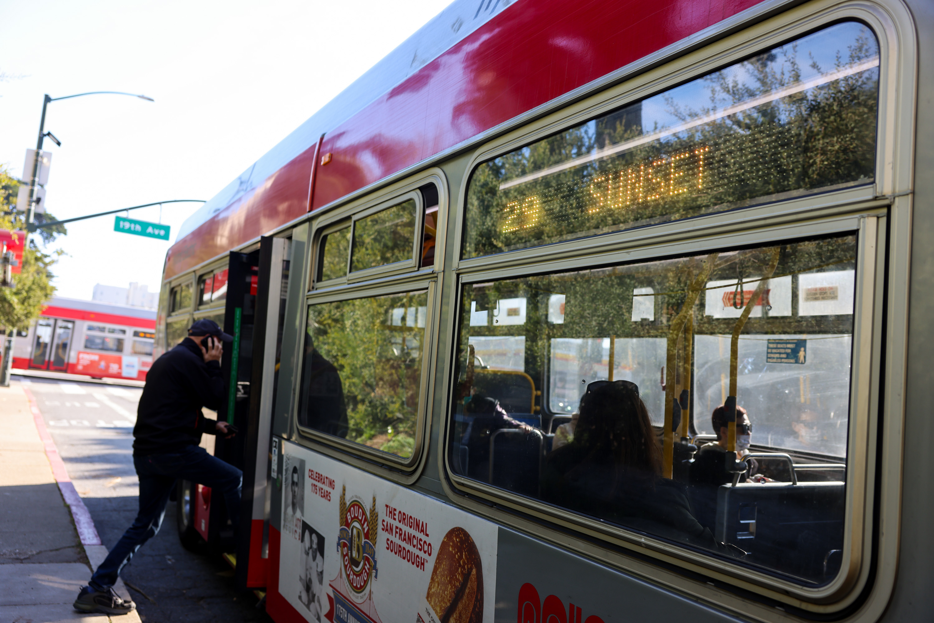 A person is boarding a city bus in San Francisco, labeled "29 Sunset." The bus is silver and red, with an advertisement for San Francisco sourdough bread.