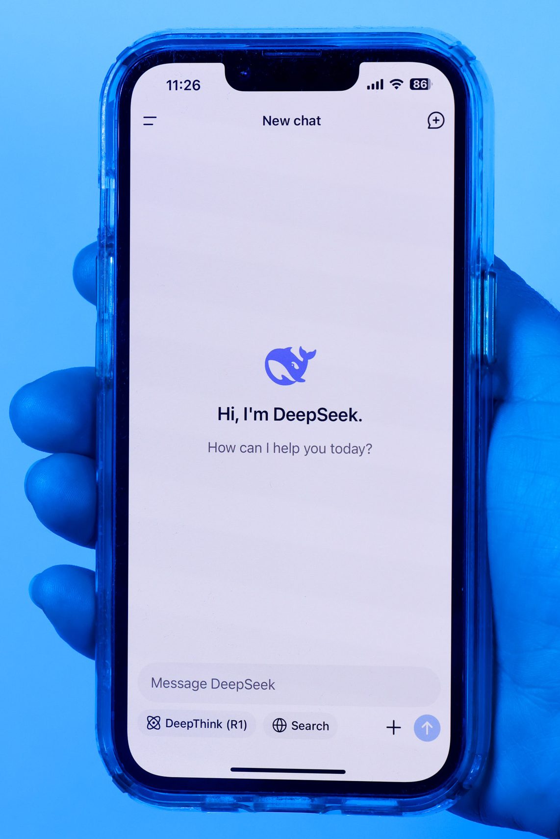 A hand holds a smartphone displaying a chat interface with "Hi, I'm DeepSeek. How can I help you today?" on the screen, set against a blue background.