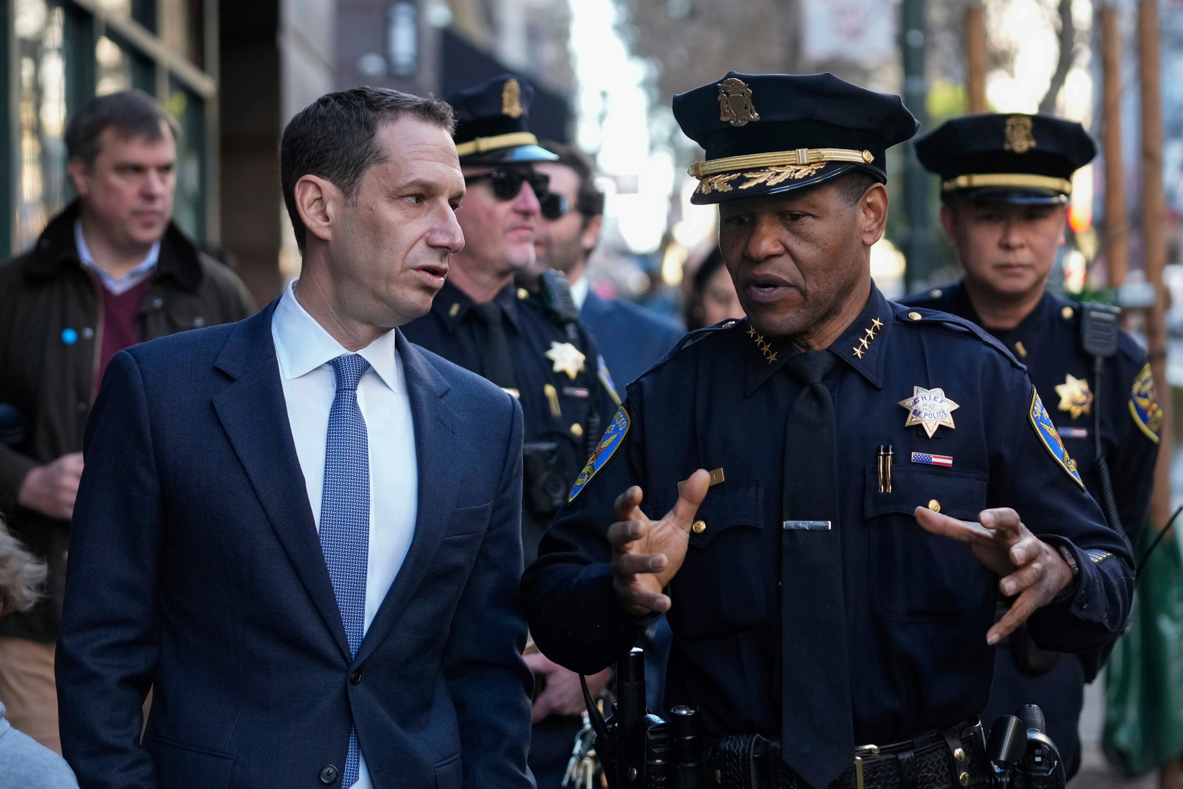 Mayor Daniel Lurie and SFPD Chief Bill Scott face each other and talk while walking.