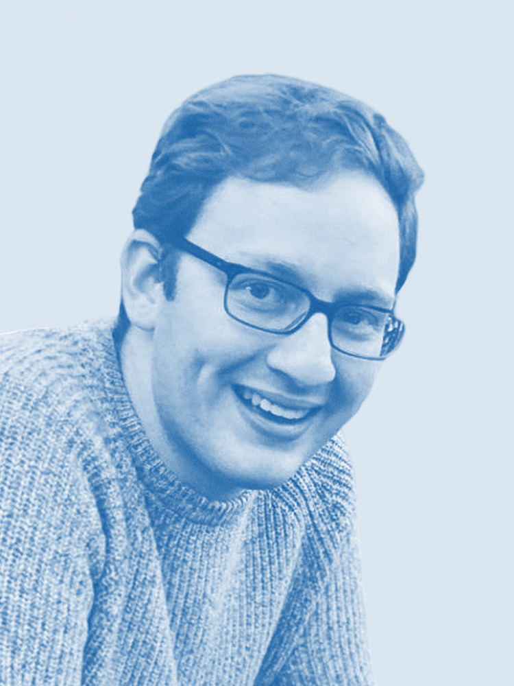 A person with glasses is smiling while wearing a knitted sweater. The image has a blue tint, giving it a monochrome appearance.