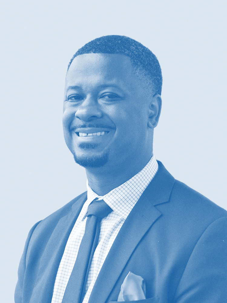 A man in a suit and tie smiles warmly. The image is in a cool, blue tone, creating a monochromatic effect. He appears confident and professional.