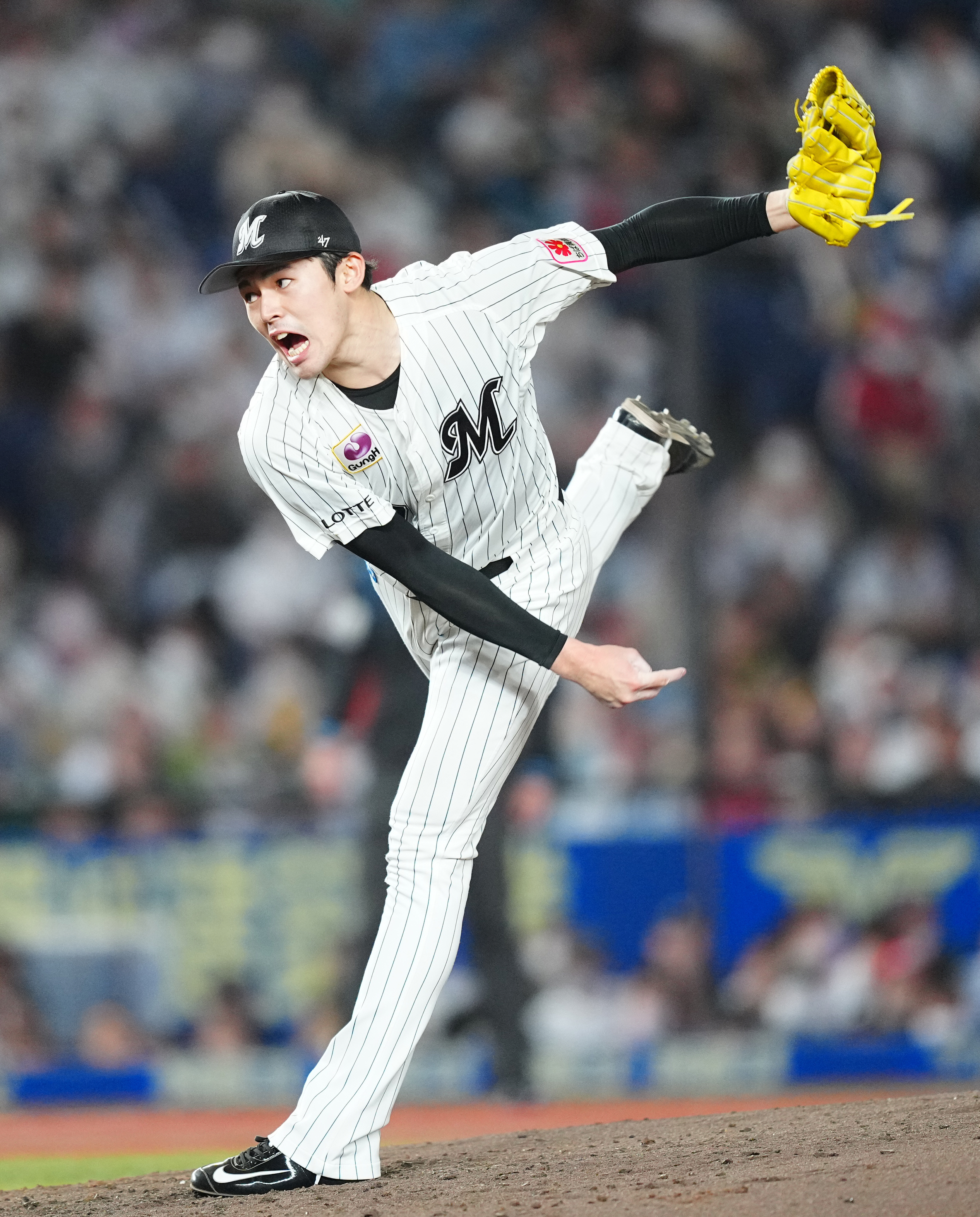 A baseball pitcher in a white pinstripe uniform and black cap is in mid-pitch, with one leg raised high and a yellow glove on his hand. The crowd is blurred behind.