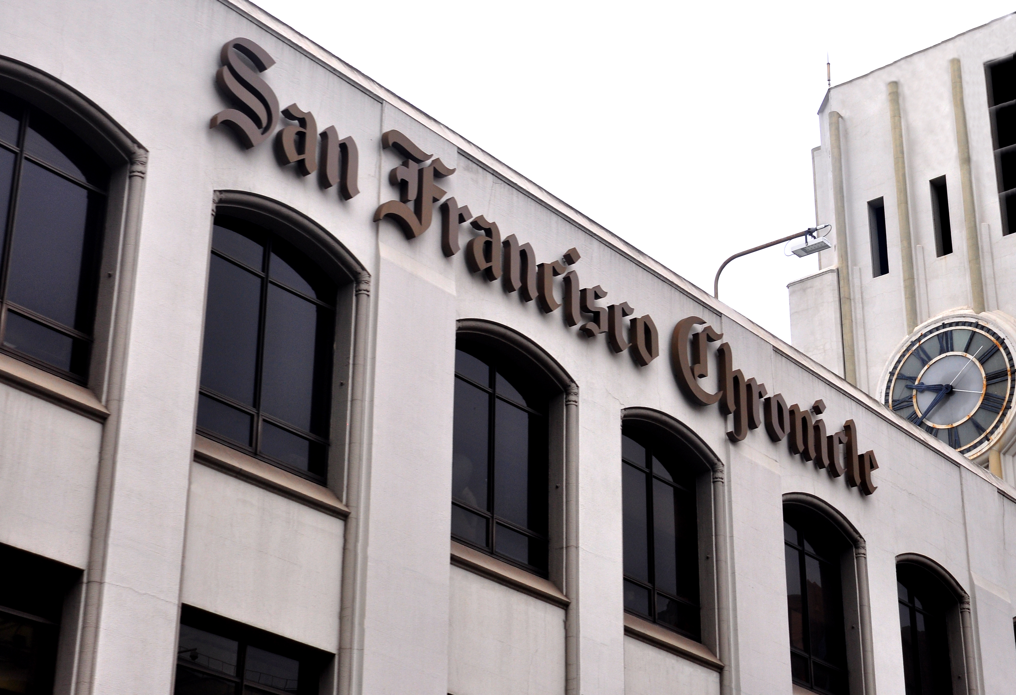 The image shows the facade of the "San Francisco Chronicle" building with arched windows and a vintage clock on the right.