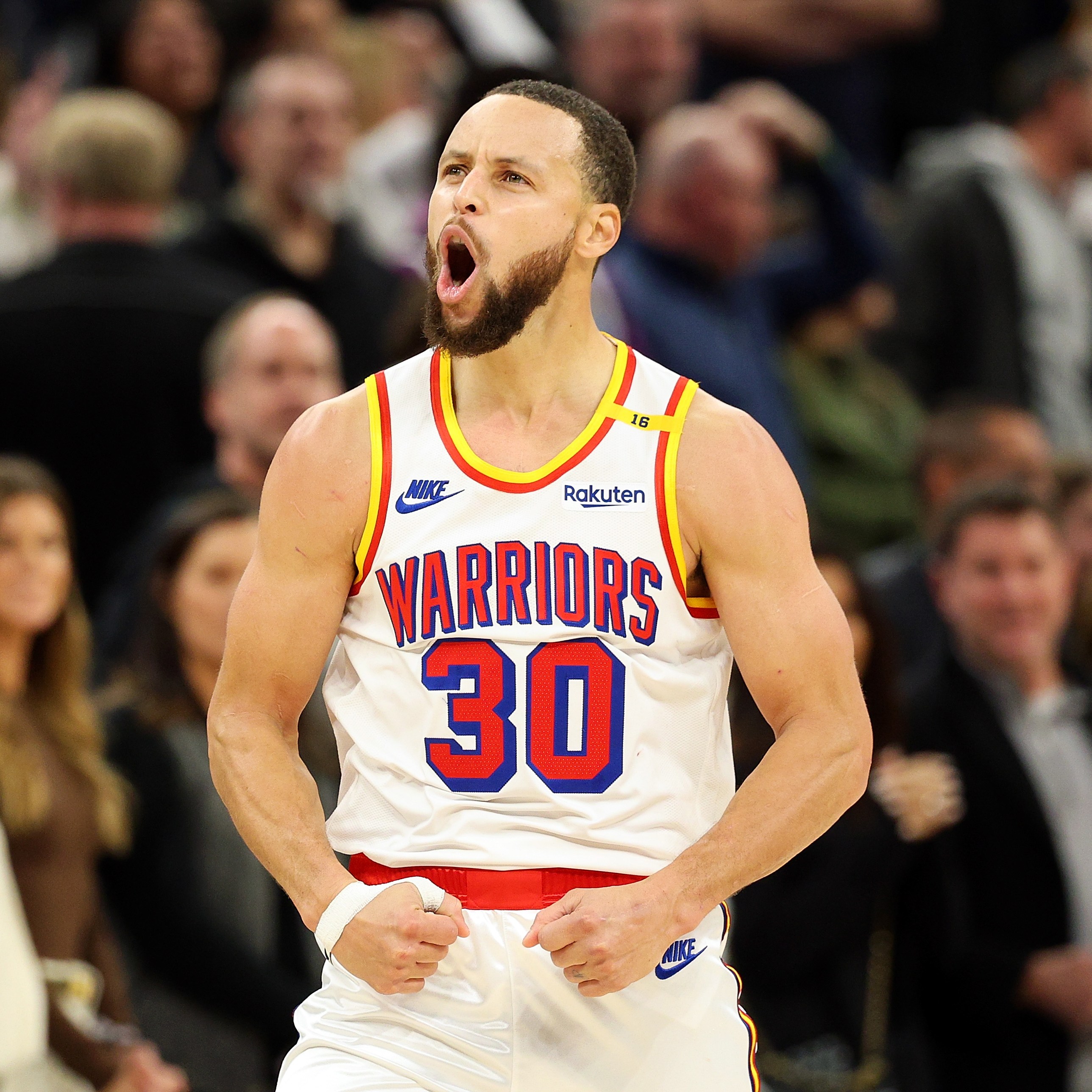 A basketball player in a "Warriors" jersey with number 30 celebrates energetically on a court, surrounded by a blurred crowd in the background.