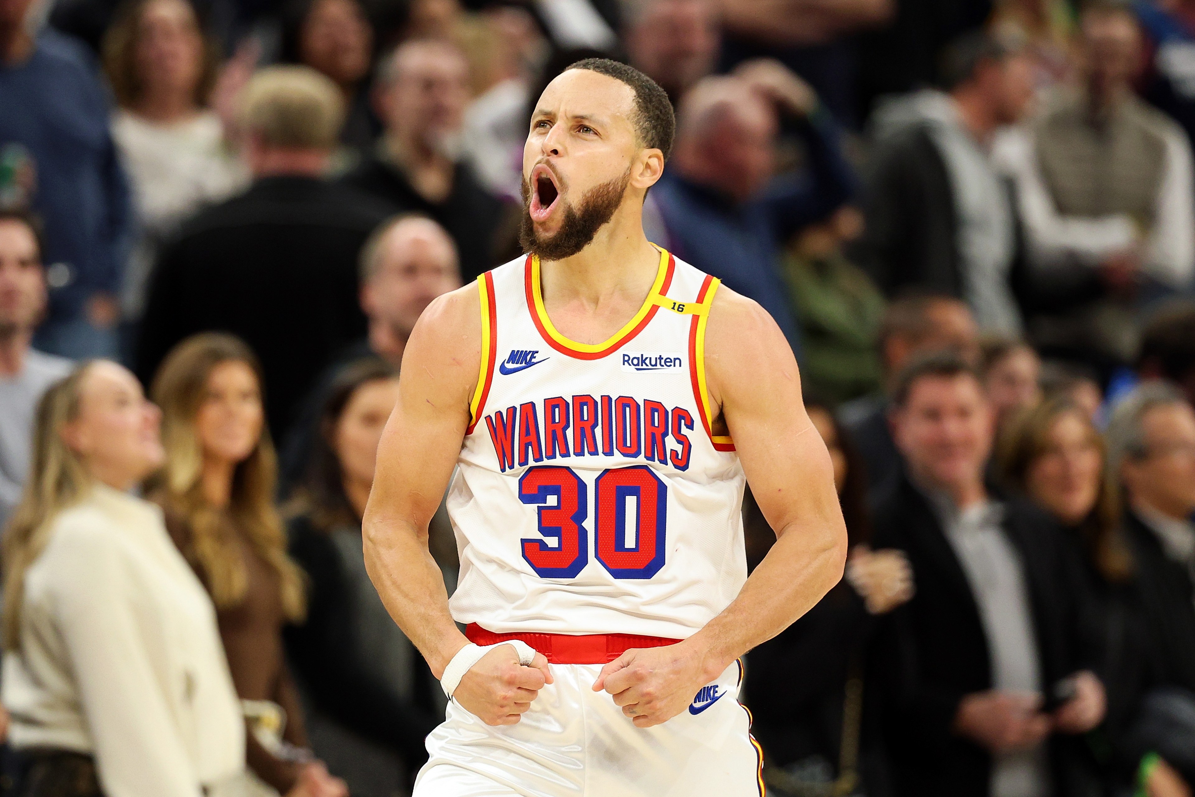 A basketball player in a "Warriors" jersey with number 30 celebrates energetically on a court, surrounded by a blurred crowd in the background.