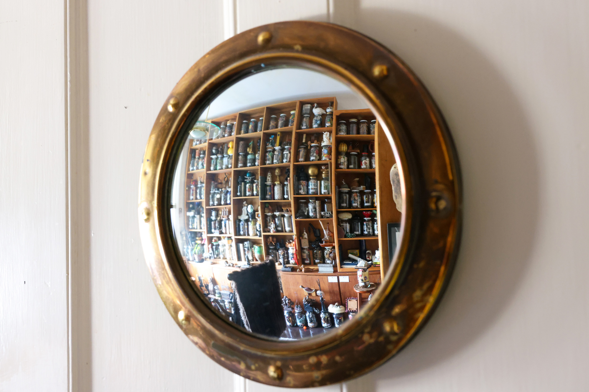 A round, brass-framed mirror reflects shelves filled with numerous jars and bottles, creating a cluttered yet intriguing vintage atmosphere.