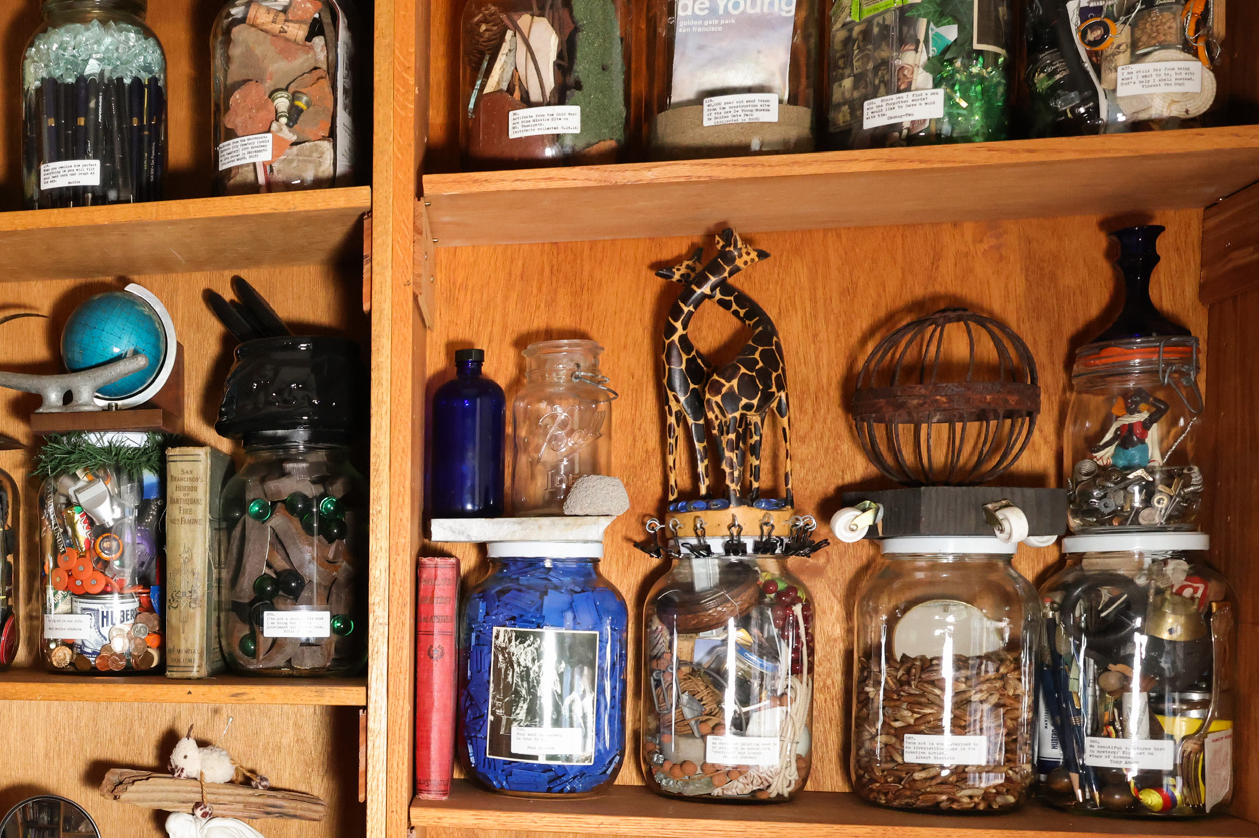 A wooden cabinet displays various jars filled with eclectic items, like pens, marbles, and small figures. Decorative objects include a globe and giraffe figures.