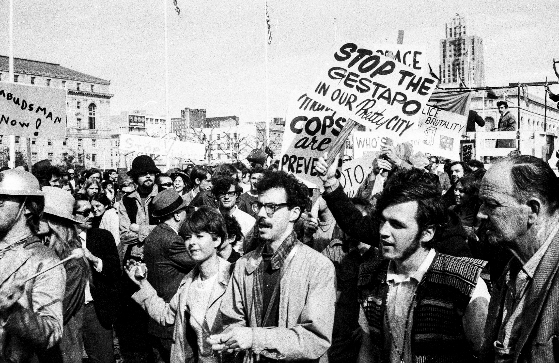 A crowd of people at a protest hold signs with messages like &quot;Stop the Gestapo&quot; and &quot;Ombudsman Now,&quot; expressing opposition to police brutality.