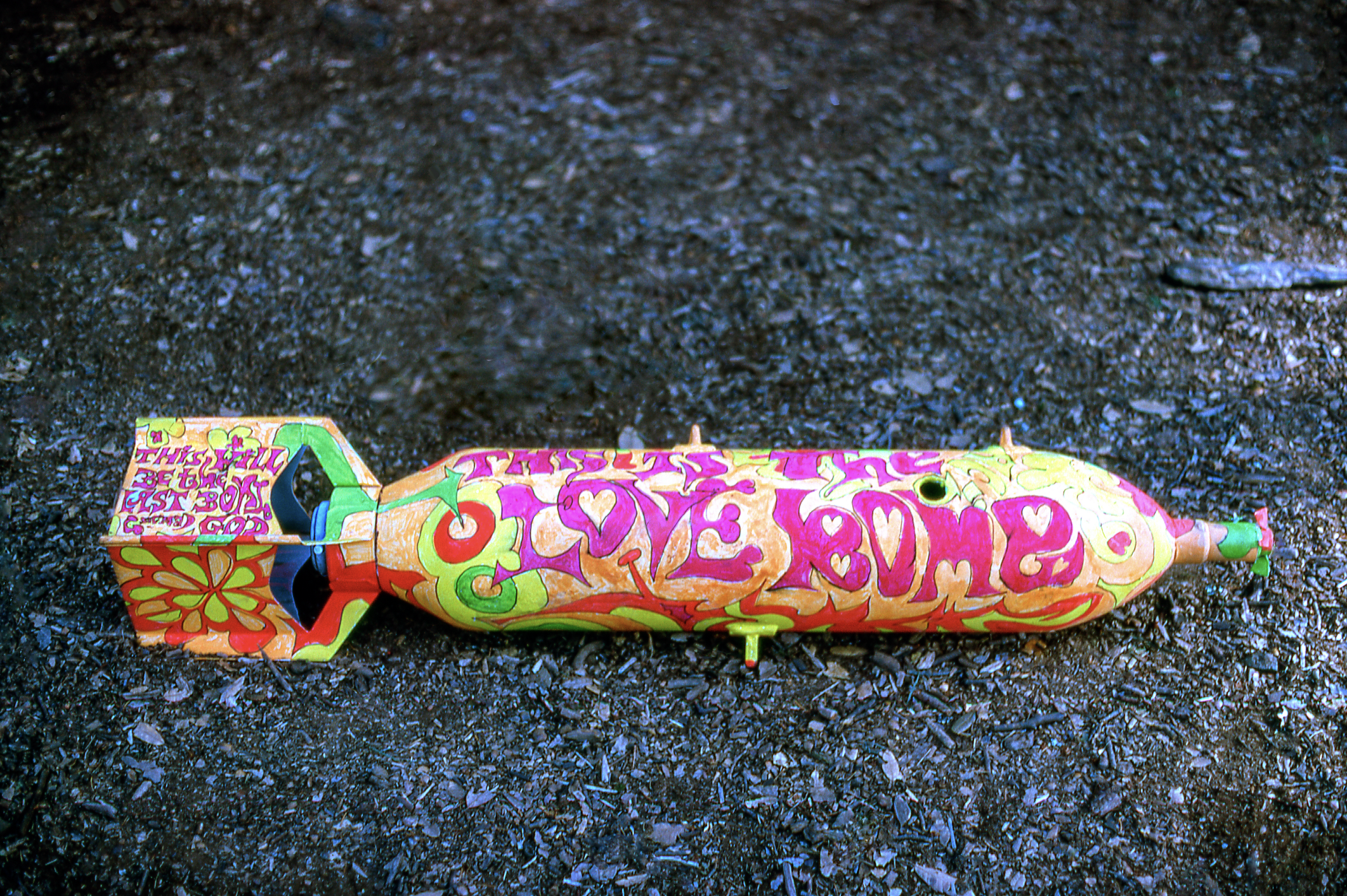 A colorful bomb-shaped object lies on the ground, covered in vibrant graffiti with words like &quot;Love Bomb&quot; in large, stylized letters.