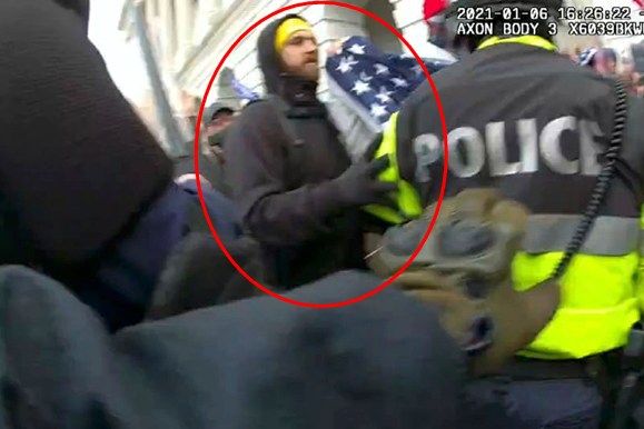 A person in a yellow hat holds a flag beside a police officer in a reflective jacket amidst a crowded scene. The timestamp and "AXON BODY" are visible.