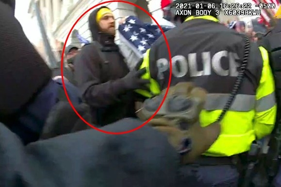 A person in a yellow hat holds a flag beside a police officer in a reflective jacket amidst a crowded scene. The timestamp and "AXON BODY" are visible.