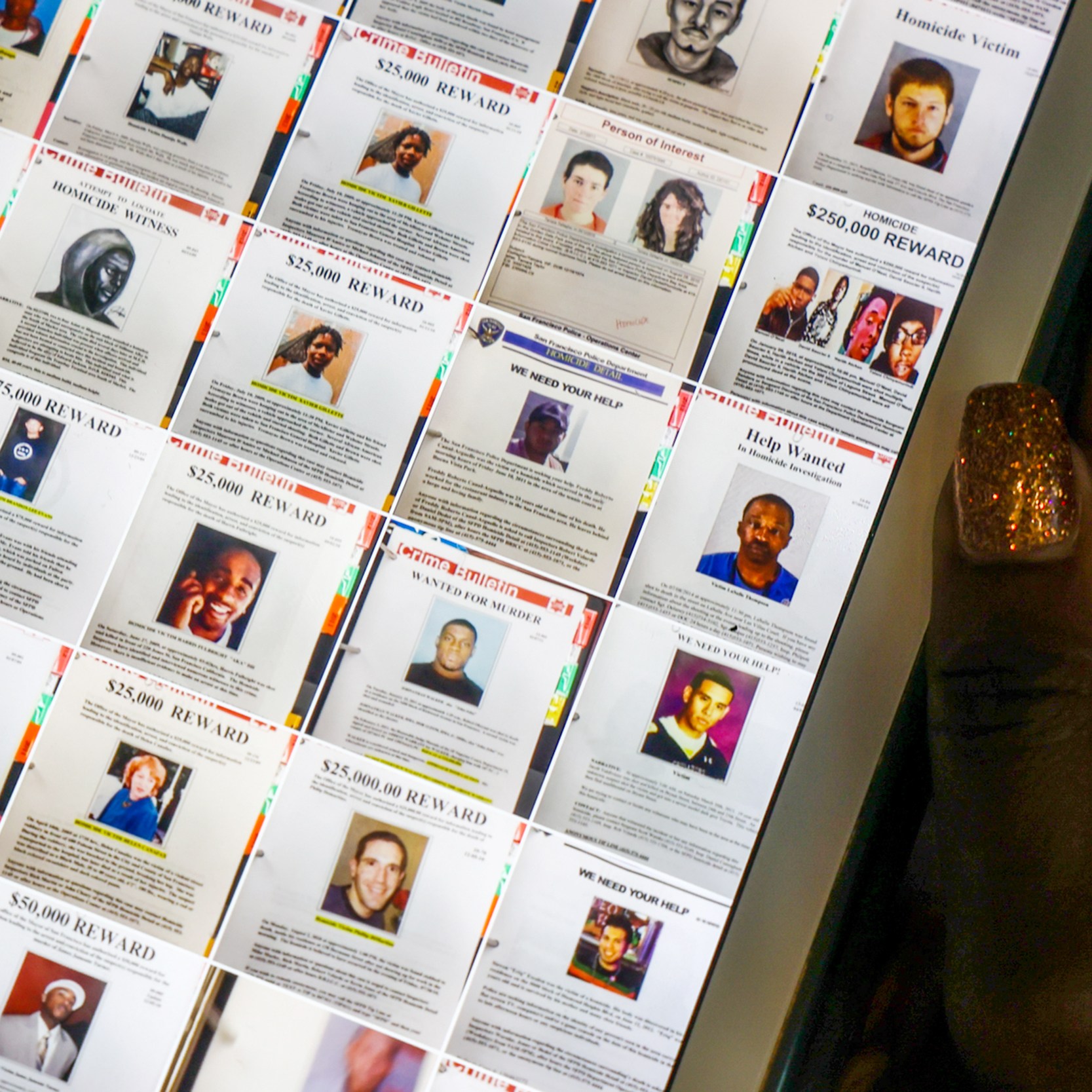 The image shows a computer screen displaying various wanted posters with photos and reward amounts. A hand with glittery nails is holding the screen.