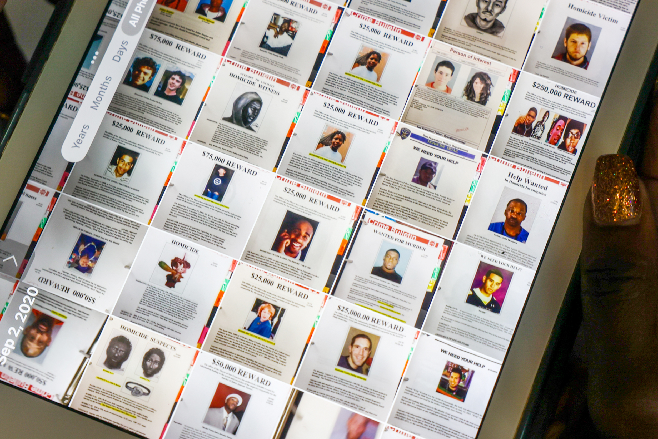 The image shows a computer screen displaying various wanted posters with photos and reward amounts. A hand with glittery nails is holding the screen.