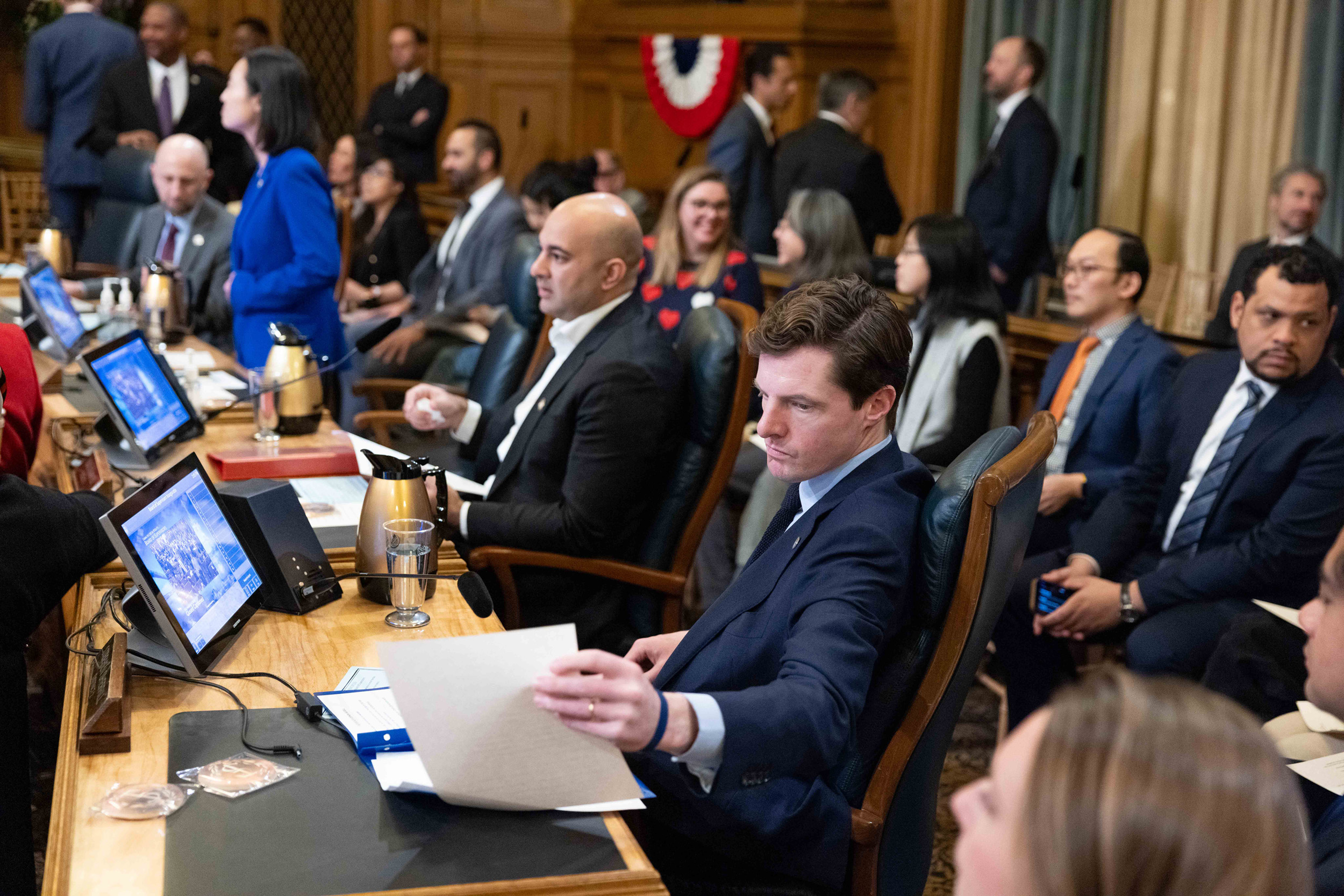 Men sit at a table in an orange wooden board room.