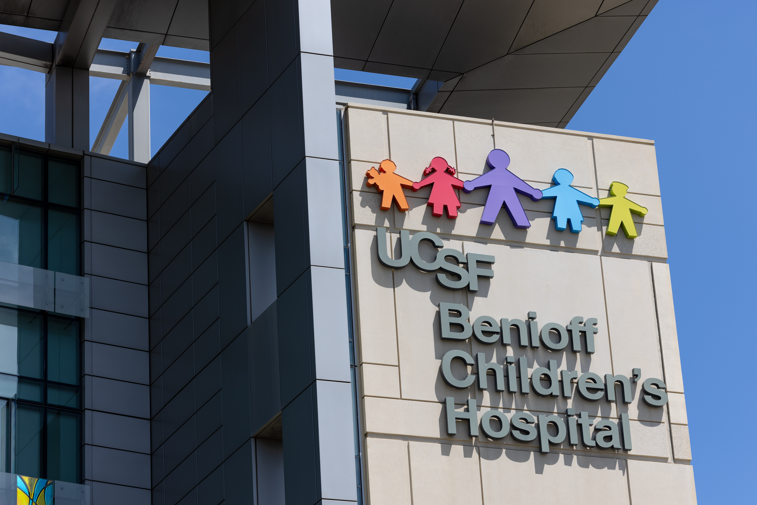 The image shows the exterior sign of UCSF Benioff Children's Hospital, featuring colorful children-shaped figures holding hands above the text.