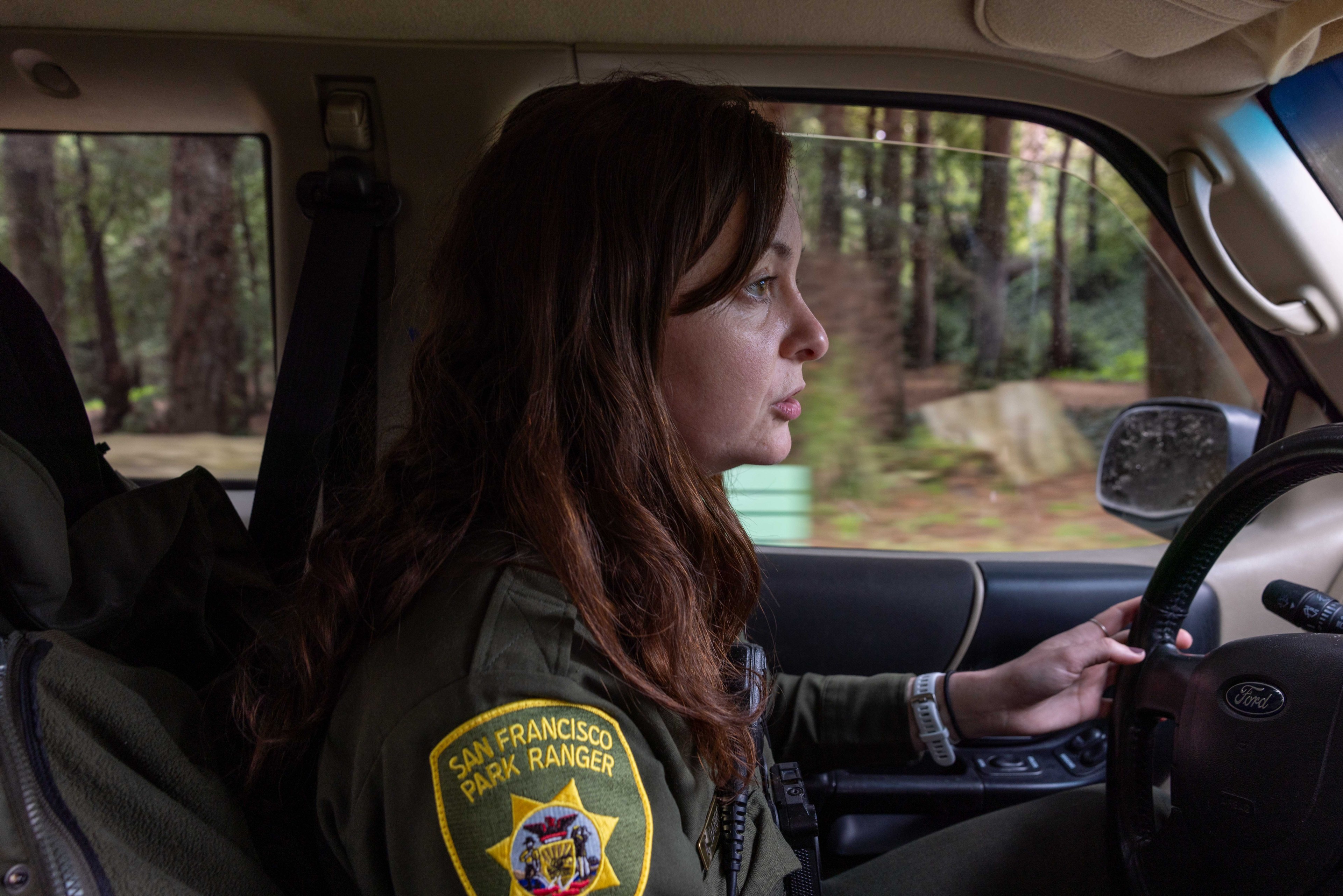 A person wearing a San Francisco Park Ranger uniform is driving a vehicle. The scene outside the window shows trees and greenery, suggesting a natural setting.