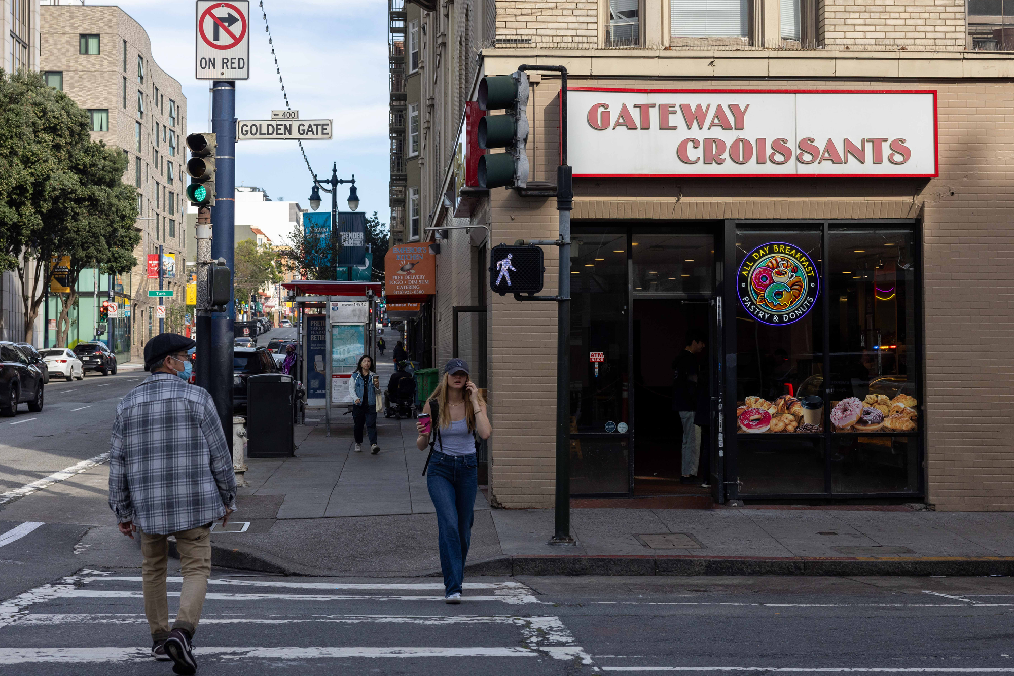 A street scene shows a man approaching a crosswalk and a woman walking with a drink. A pastry shop, &quot;Gateway Croissants,&quot; is visible on the corner.