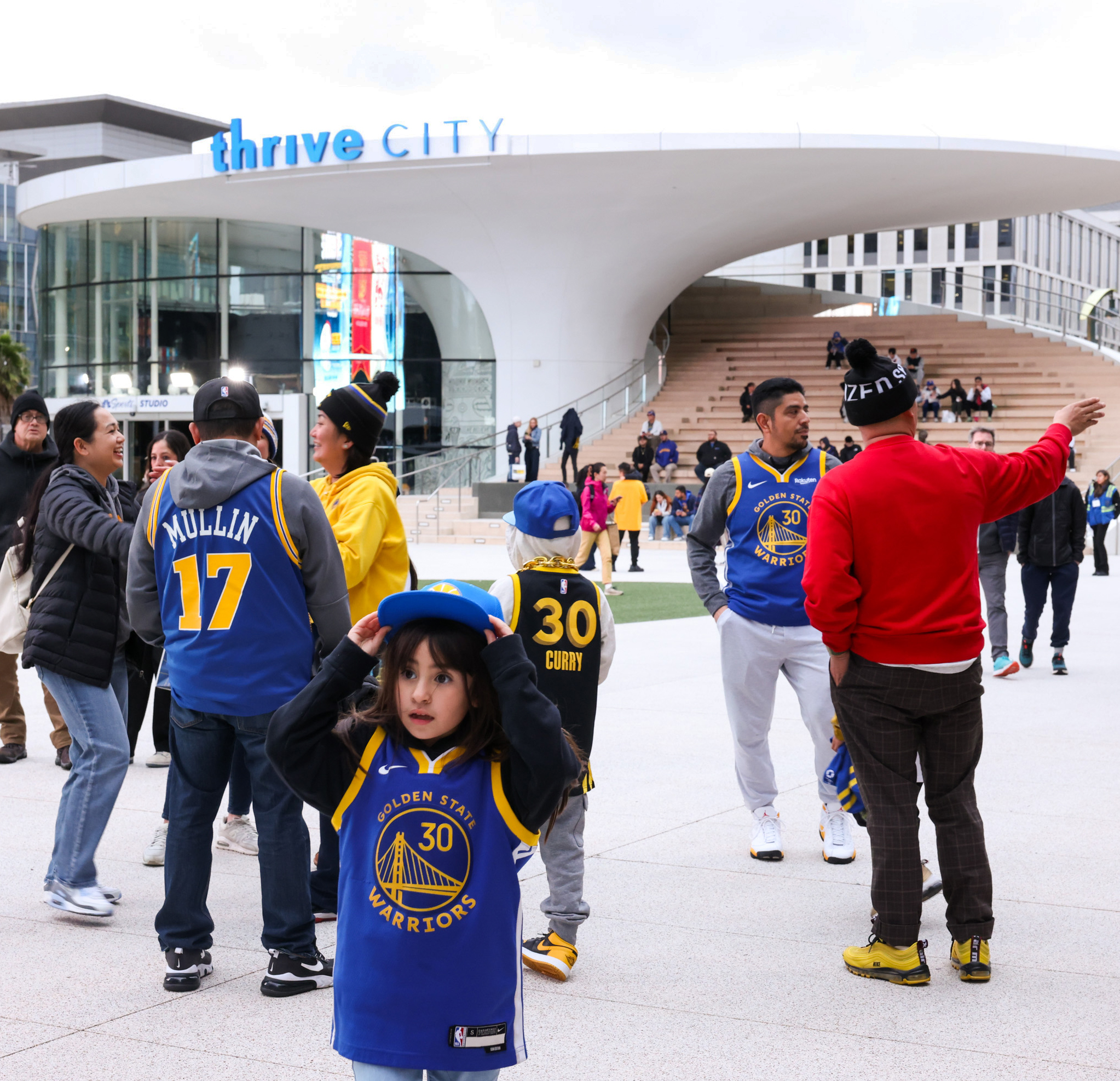 People wearing Golden State Warriors jerseys socialize outside the Thrive City arena. Among them are children dressed in jerseys with the number 30.