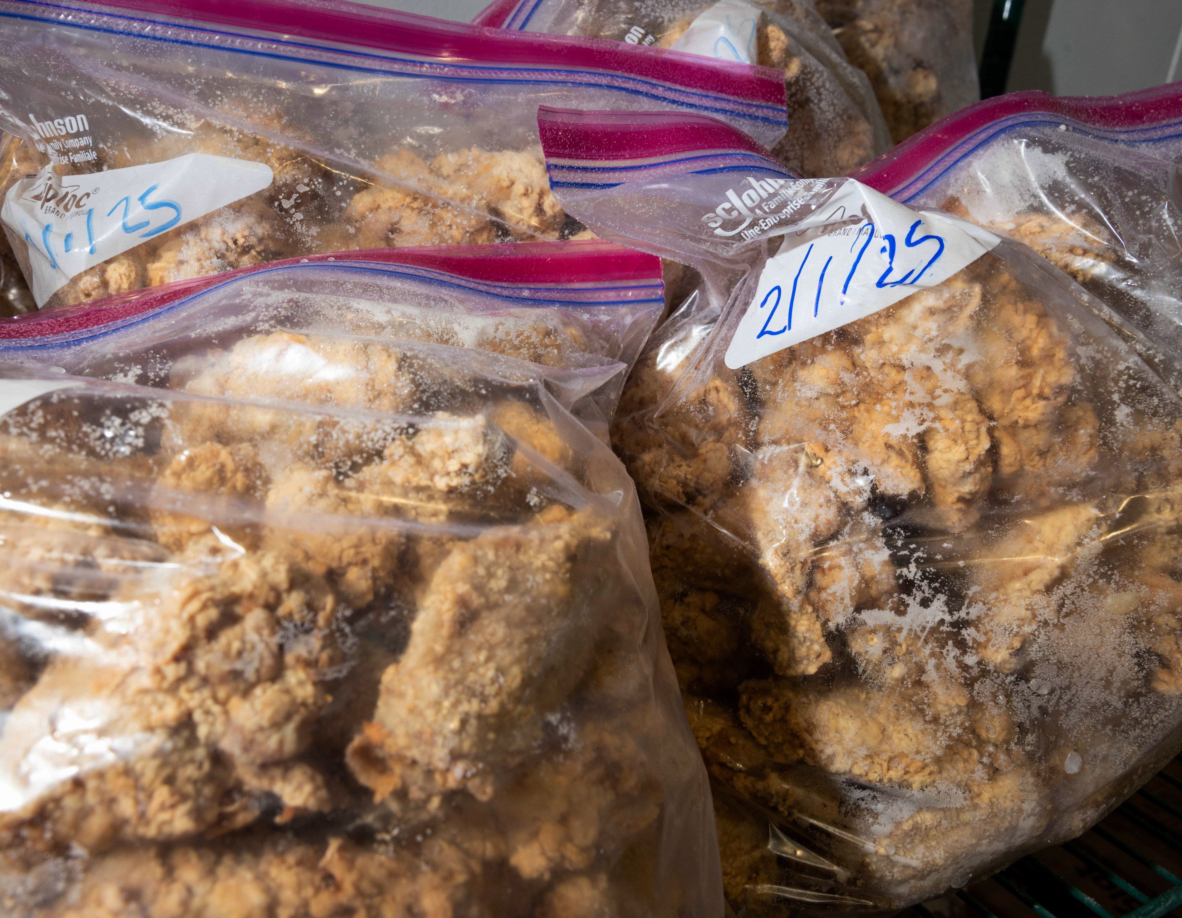 Plastic bags filled with frozen, breaded items are stacked. The bags have handwritten dates on labels and show frost inside.