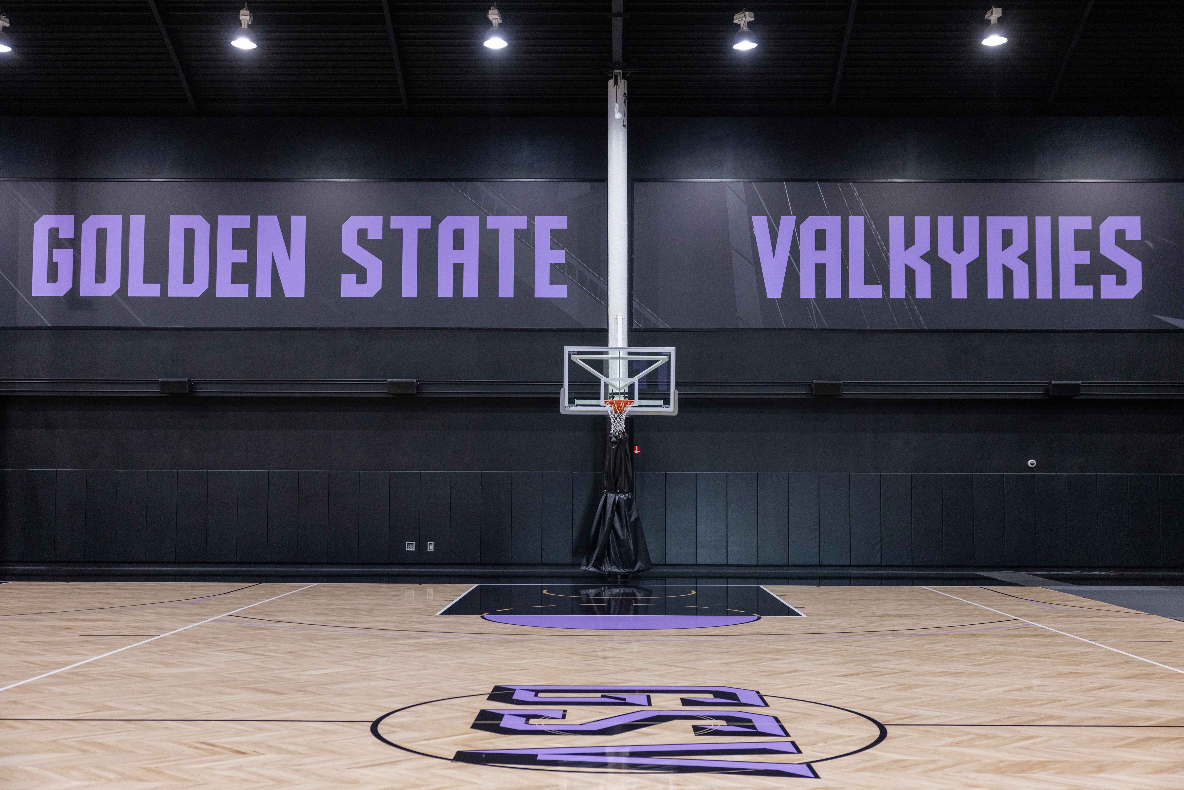 A basketball court with a hoop is centered against a black wall. The text &quot;GOLDEN STATE VALKYRIES&quot; is displayed in large purple letters above.