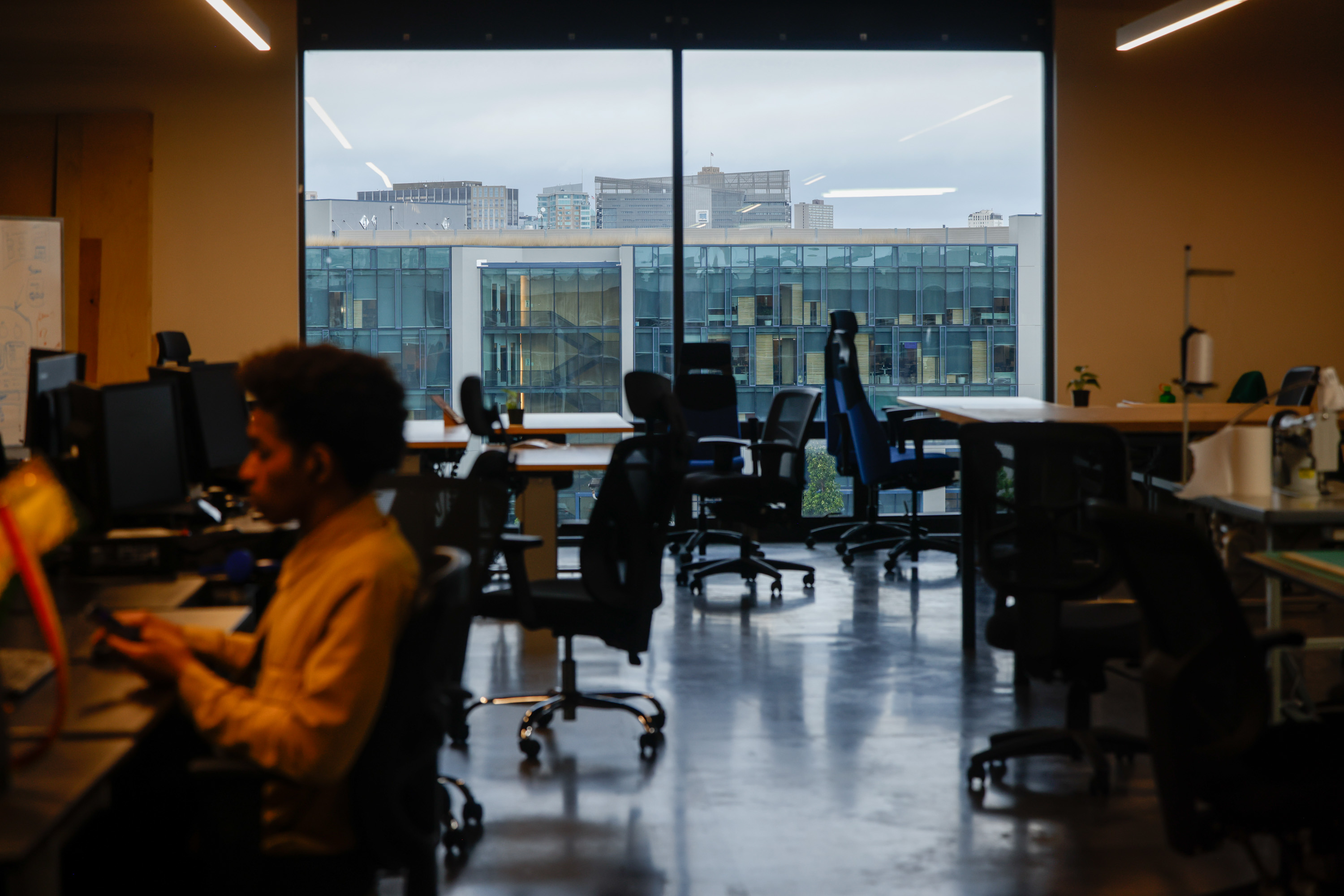 A person works at a computer in a dark room of other empty office chairs and work tables at Humanmade.