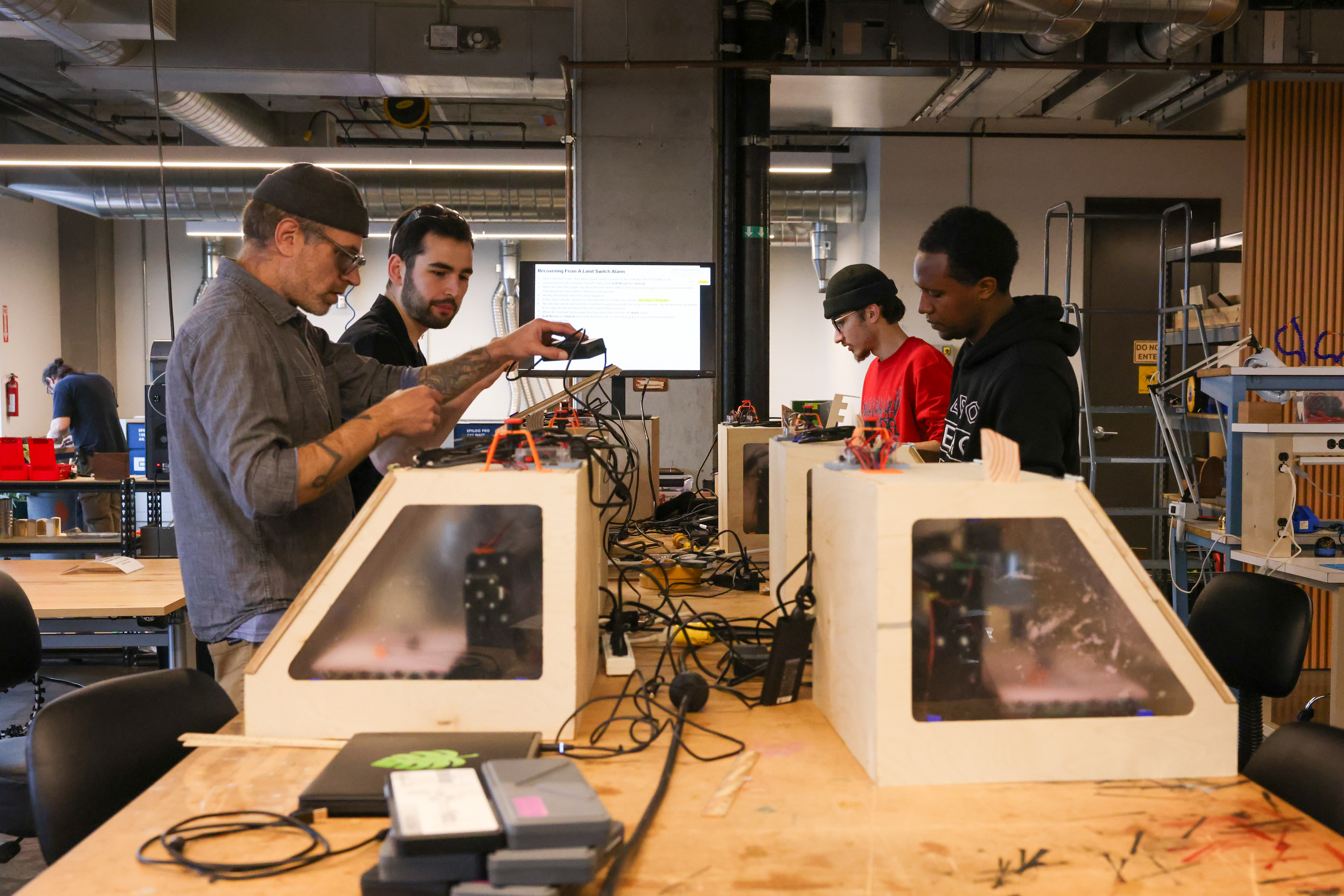 Four people use CNC machines in a workroom at Humanmade.