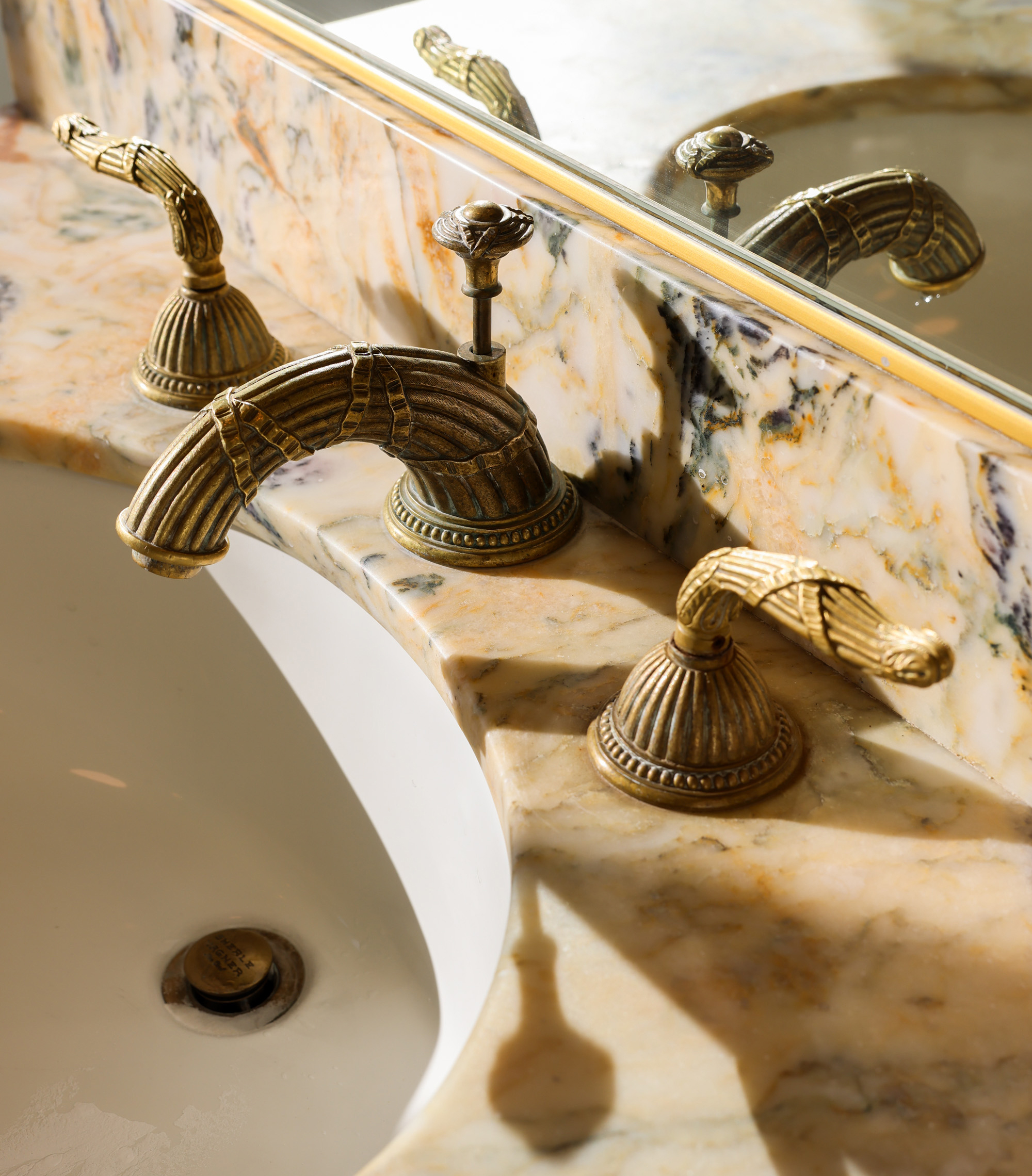 A marble sink countertop features ornate brass fixtures with intricate detailing and a mirror reflecting the faucet design.