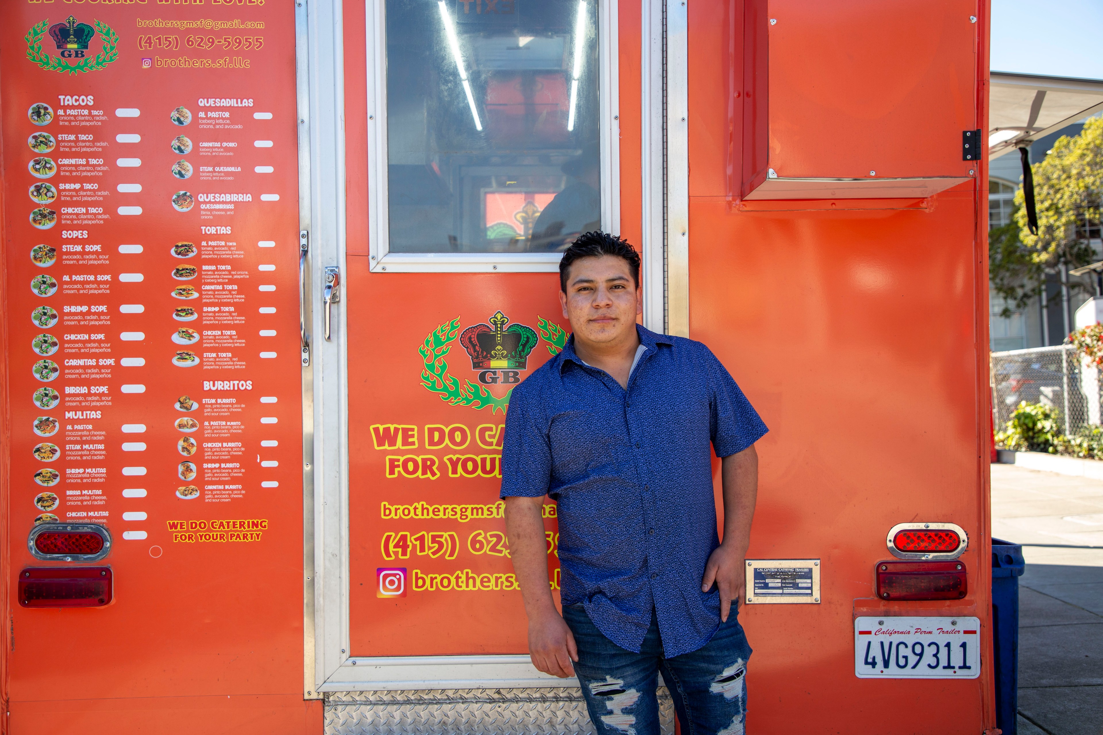 A person in a blue shirt leans against an orange food truck with a visible menu and contact details. The truck offers various Mexican dishes.