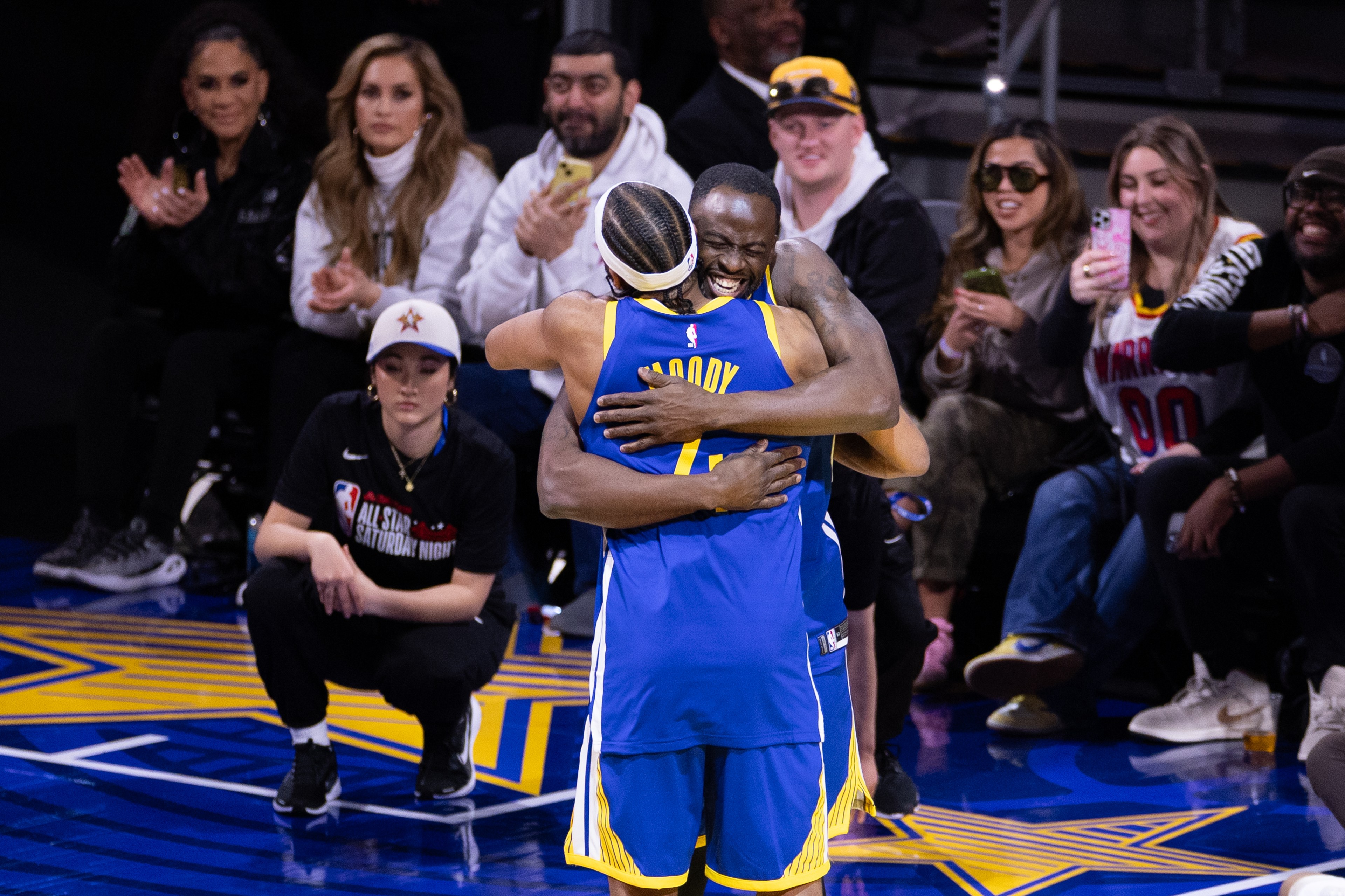 Two basketball players in blue jerseys hug on the court, surrounded by cheering spectators. One player has &quot;Moody&quot; on his jersey.