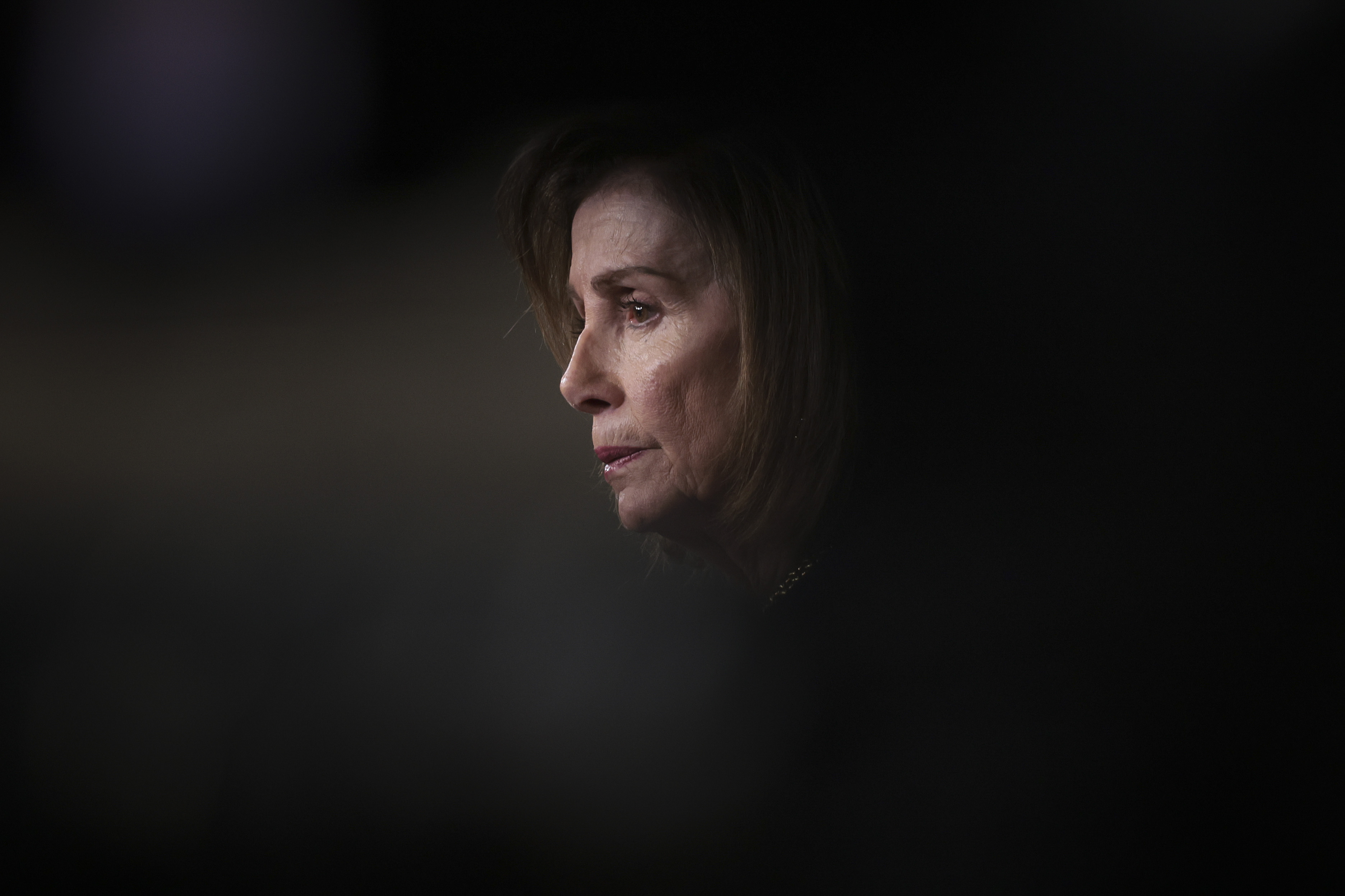 A person is seen in profile with soft lighting highlighting their face against a dark, blurred background. The expression appears contemplative.