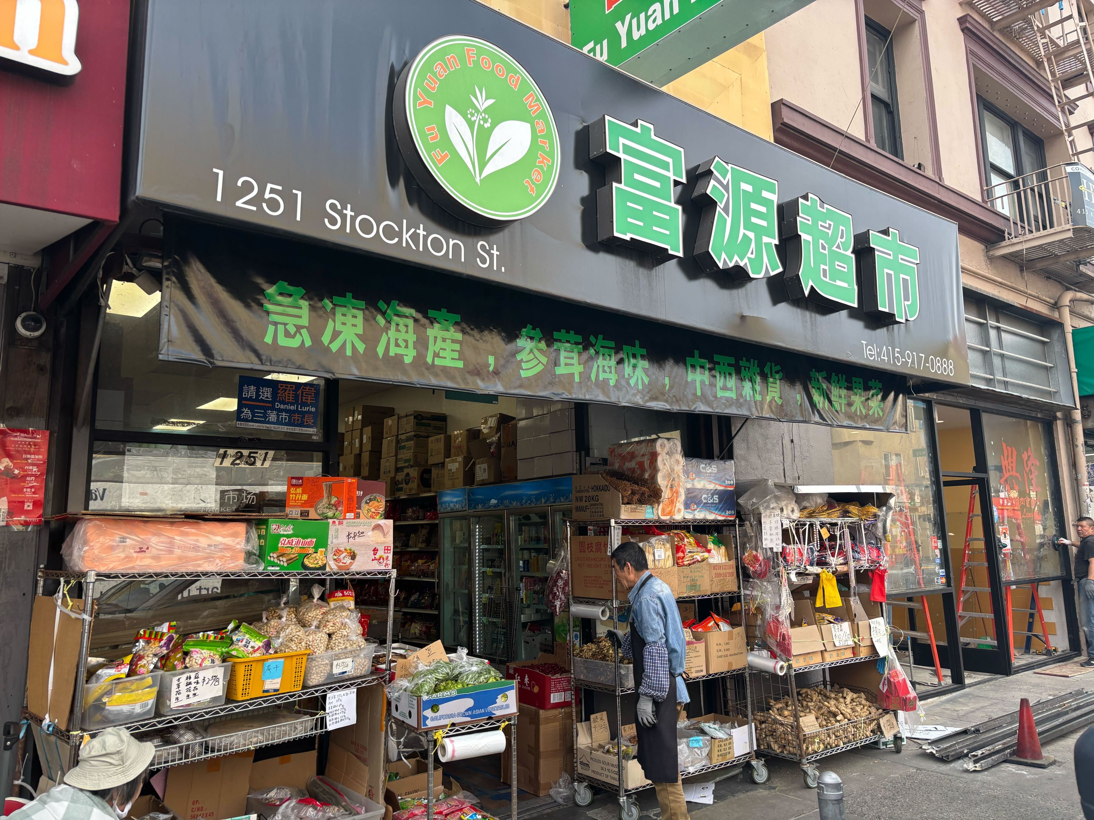 A store with a green sign displays &quot;Fu Yuan Food Market&quot; on Stockton Street. It has shelves of goods outside, and a person stands by the entrance.