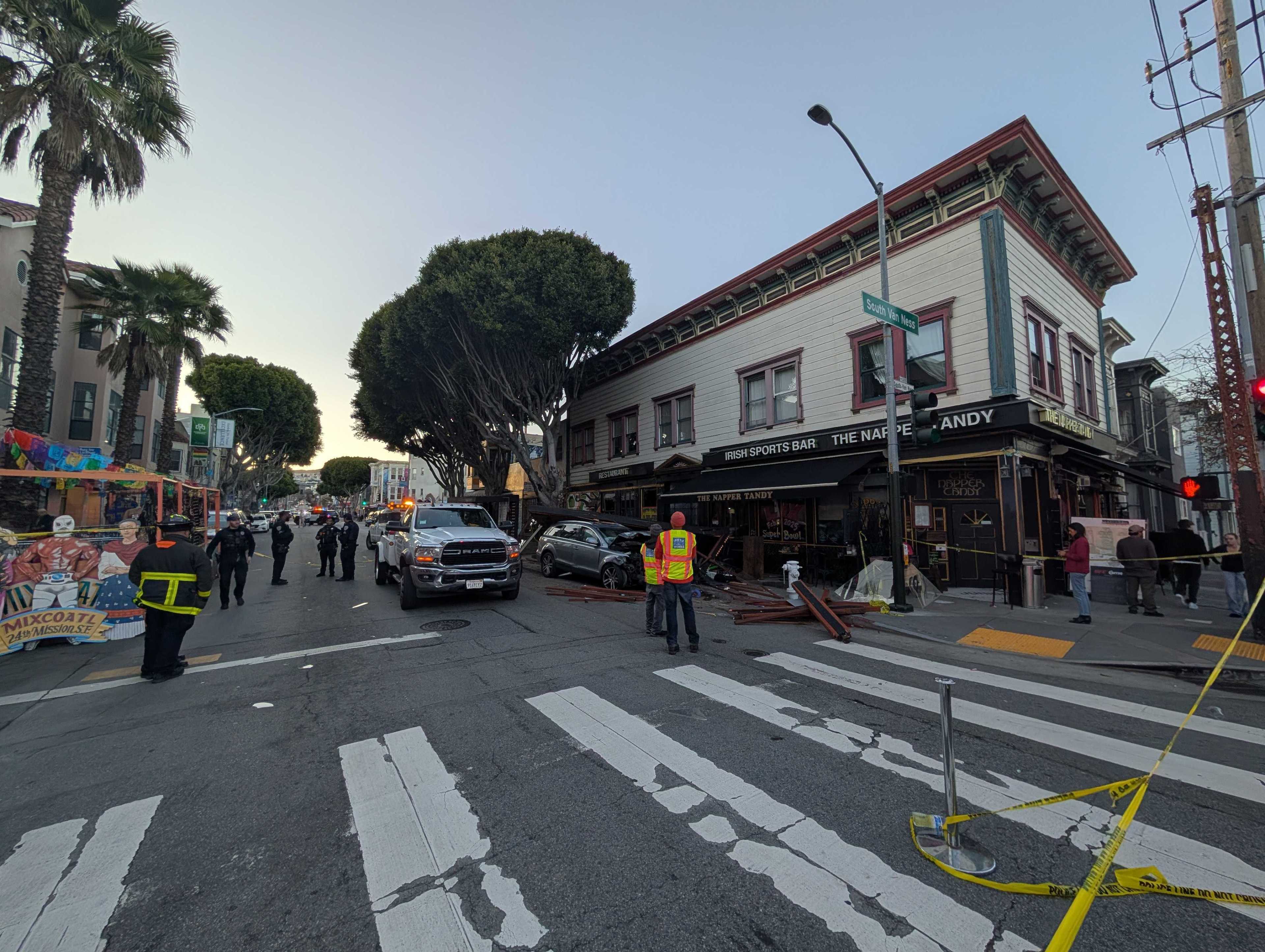 A street scene shows emergency personnel near a damaged Irish sports bar. A truck and fallen debris are present, with onlookers and caution tape around.