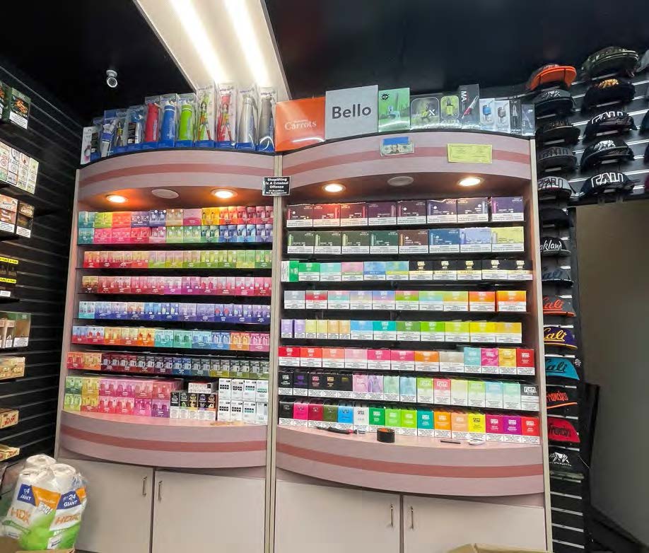 The image shows a store display with shelves full of colorful vape or e-cigarette products and accessories beneath bright lights. Hats are displayed on the right.