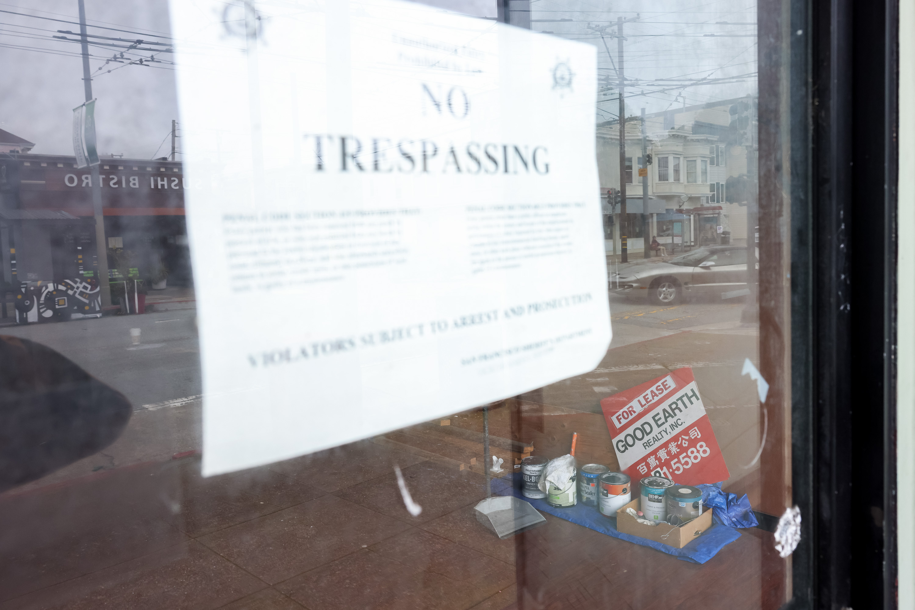 A &quot;No Trespassing&quot; sign is taped to a window. Behind the glass, paint cans and a &quot;For Lease&quot; sign from Good Earth Realty are visible.