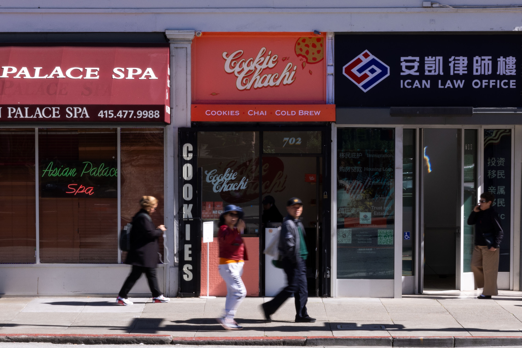 Three storefronts are visible: Asian Palace Spa with a red sign, Cookie Chachi with an orange sign, and ICAN Law Office with a blue sign. People walk by.