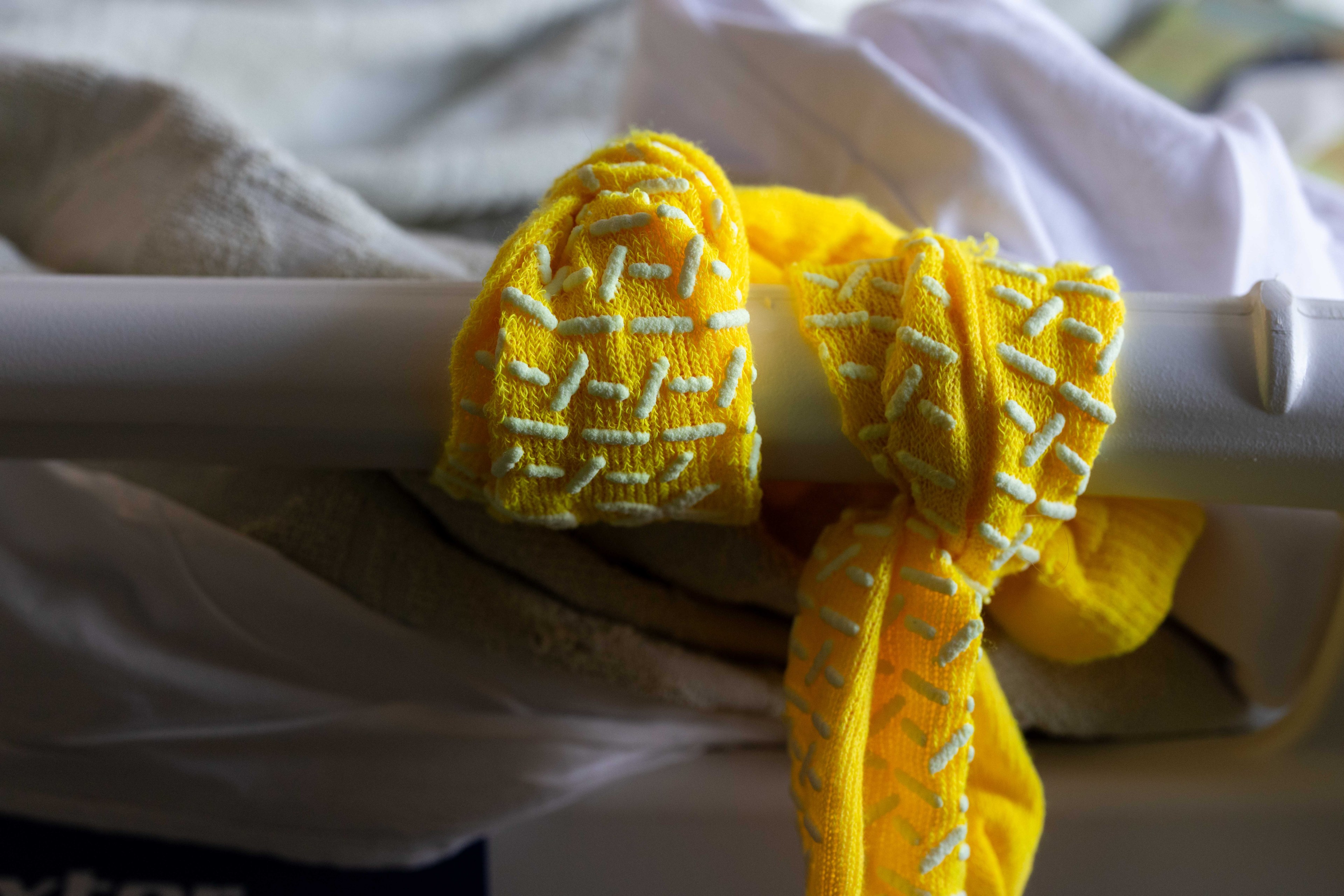 A bright yellow sock with white textured patterns hangs on a white bar, draped over a soft beige fabric.