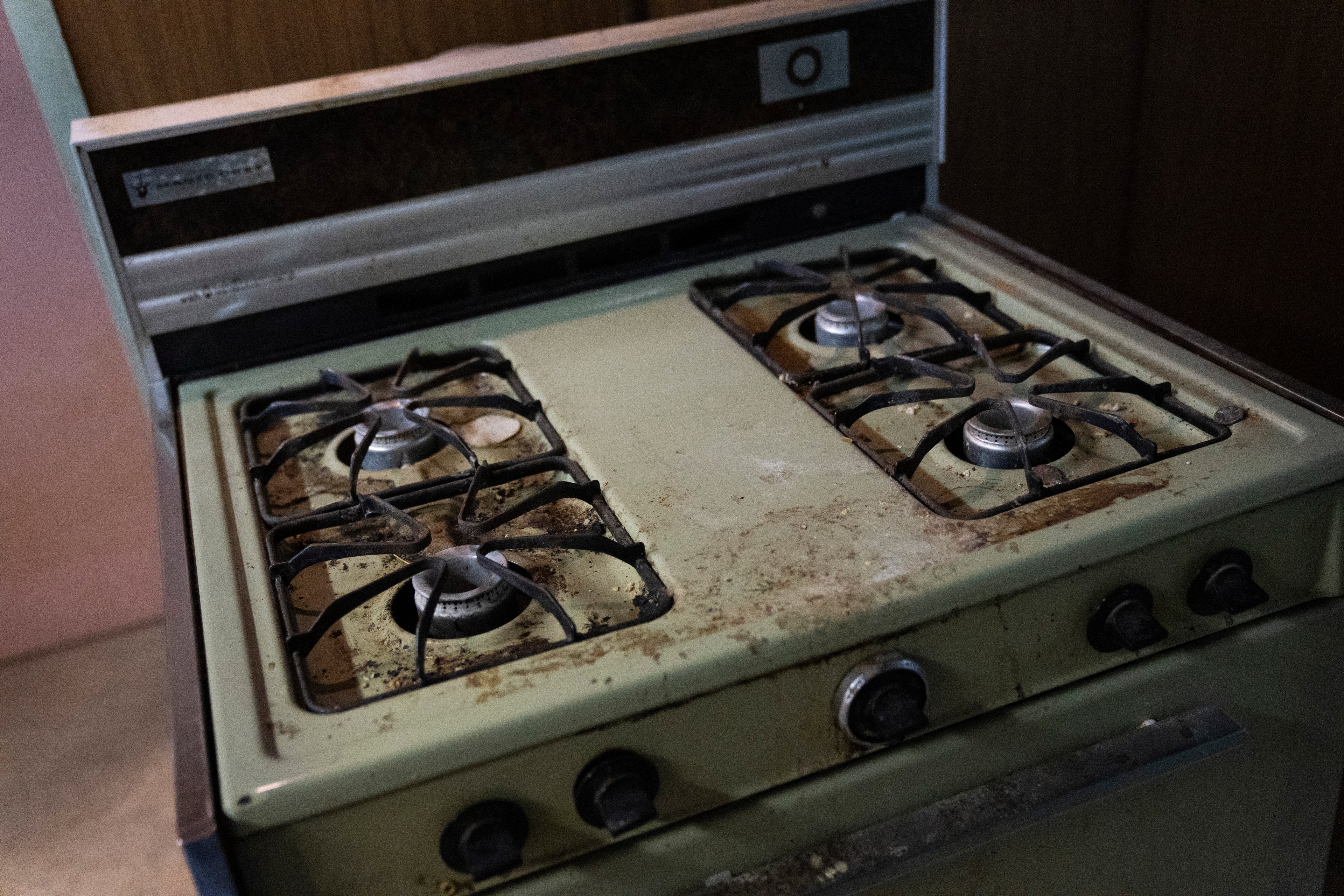 The image shows an old, dirty gas stove with four burners and grime accumulated on the green metal surface and surrounding knobs.