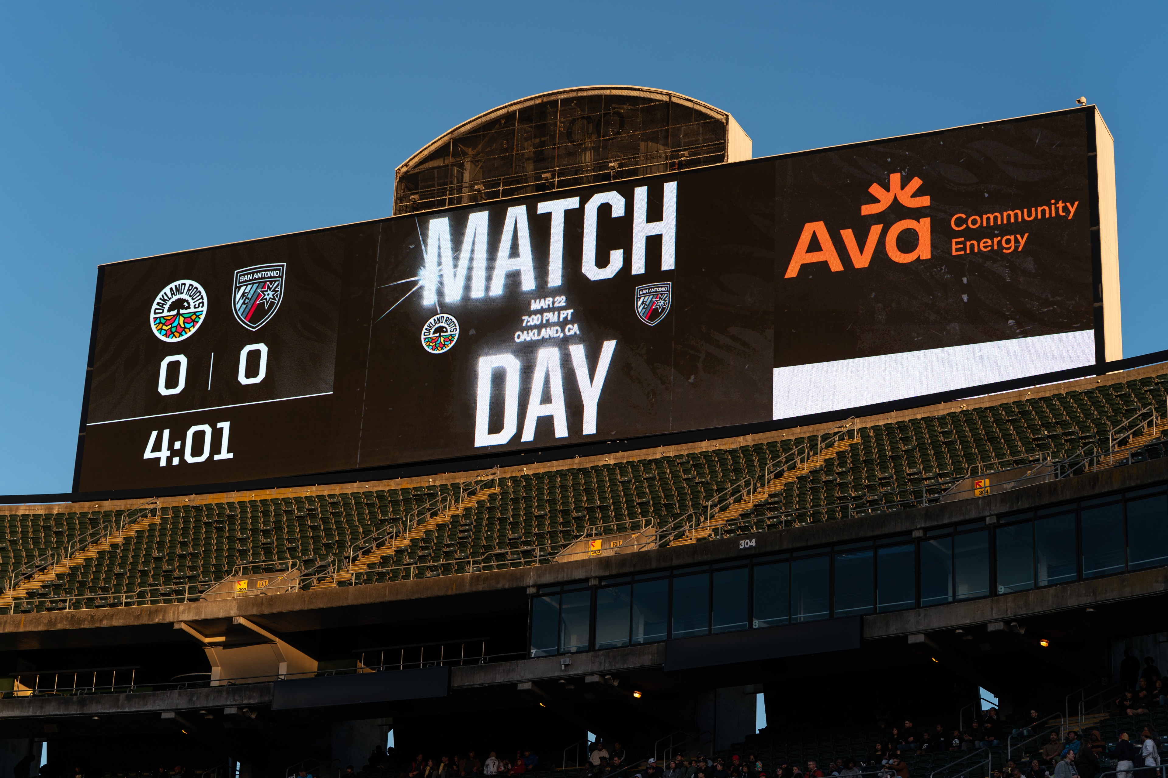 A stadium scoreboard shows &quot;MATCH DAY&quot; with two team logos, a score of 0-0, and a time of 4:01. It mentions a match at 7:00 PM PT in Oakland, CA.