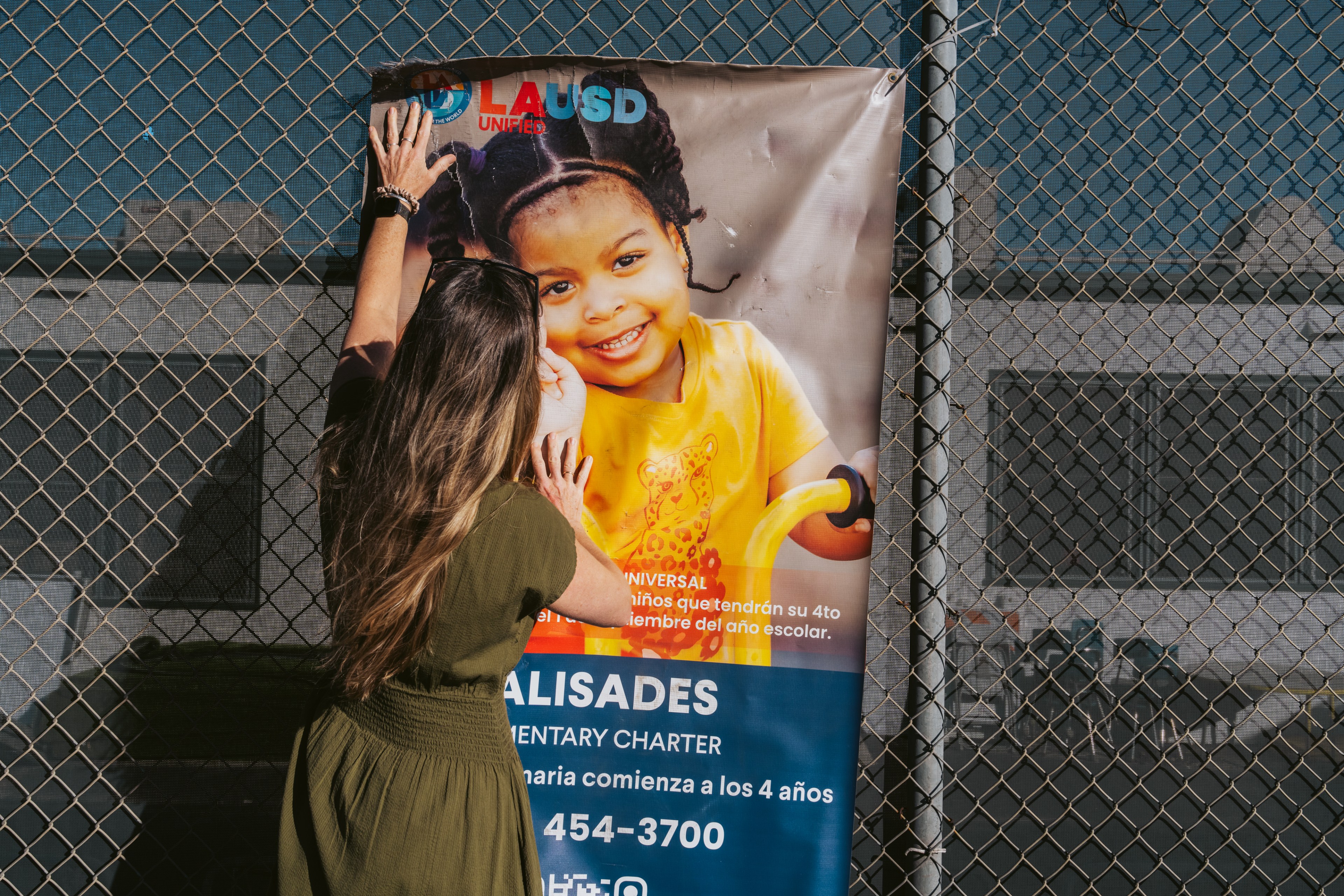 Samantha Wiesler looks at a banner hanging on Palisades Elementary Charter School’s fence in Pacific Palisades in Los Angeles on Thursday, Feb. 20, 2025.   Since losing their campus in the Palisades fire, the school was co-located with Brentwood Science Magnet Elementary.