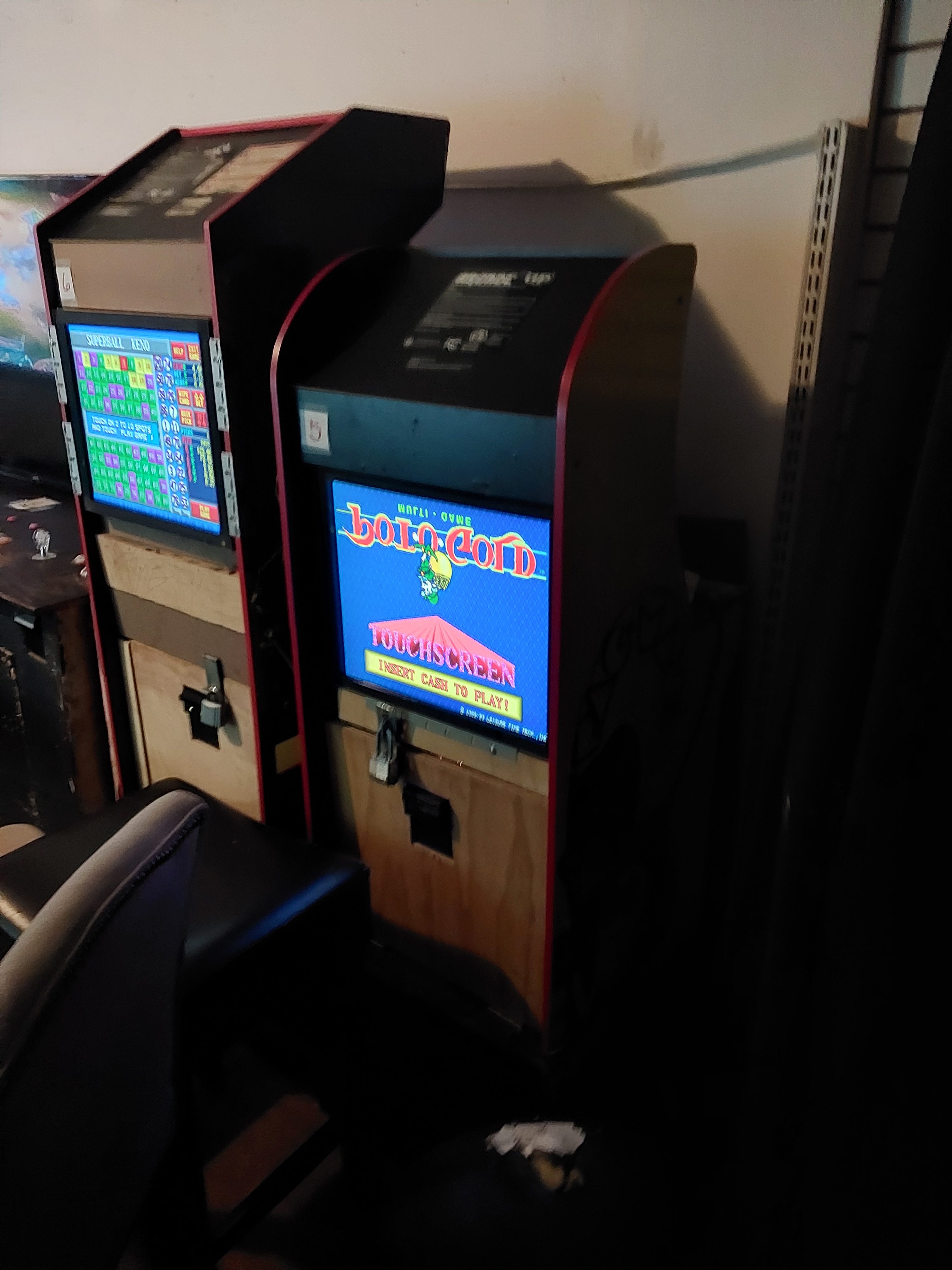 Two vintage arcade machines are shown in a dimly lit room. The right machine displays &quot;Touchscreen&quot; and an instruction to insert a card to play.