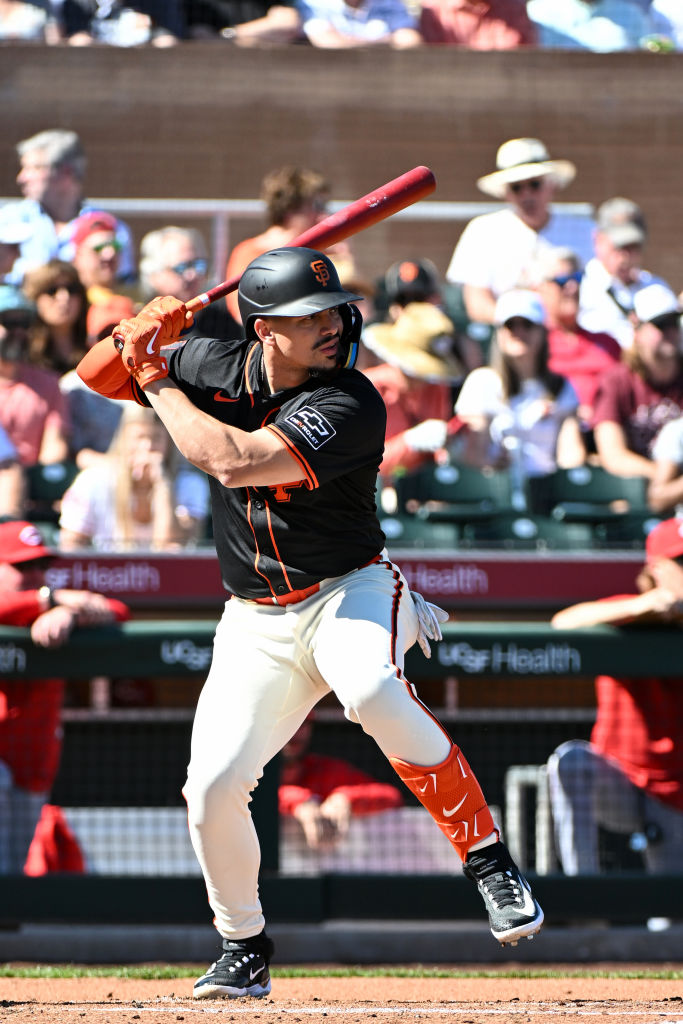 A baseball player in a black and orange uniform stands poised to swing a bat during a game, with a crowd watching in the background.