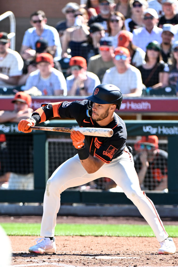 A baseball player in a black jersey and helmet is preparing to bunt the ball during a game, with a crowded stadium in the background.